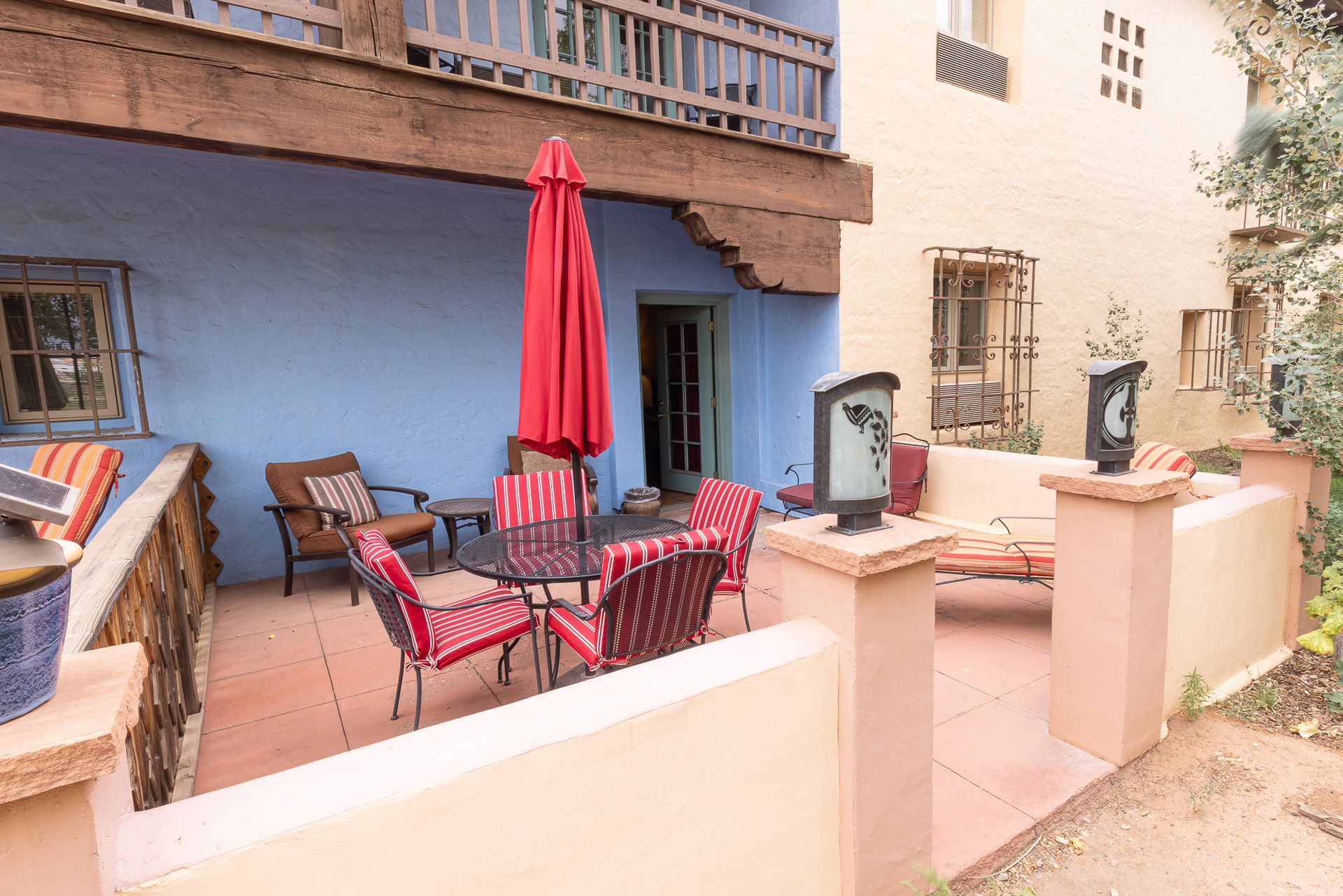 Outdoor patio with red umbrella, table, chairs, and a blue wall.