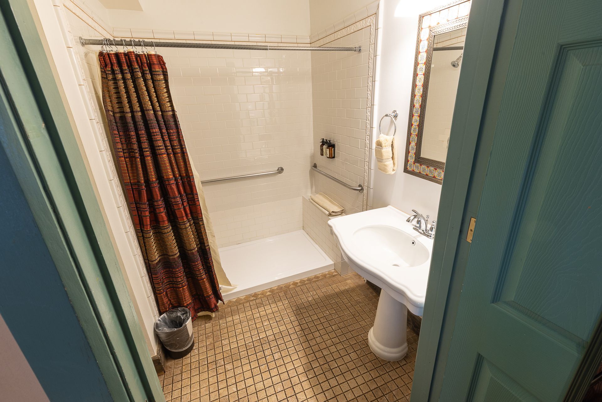 Small bathroom with a white shower, sink, and tiled floor. Maroon shower curtain, gold-framed mirror.