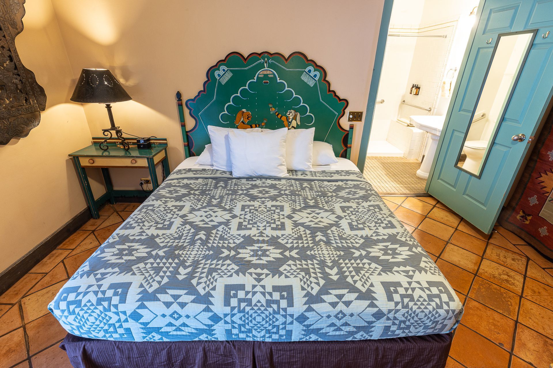 Bedroom with teal headboard, patterned blanket, turquoise nightstand, and open door to a bathroom.