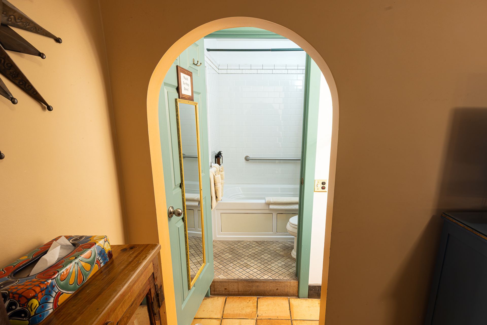 Bathroom doorway, archway opening to a white tiled shower and sink. Door is turquoise.