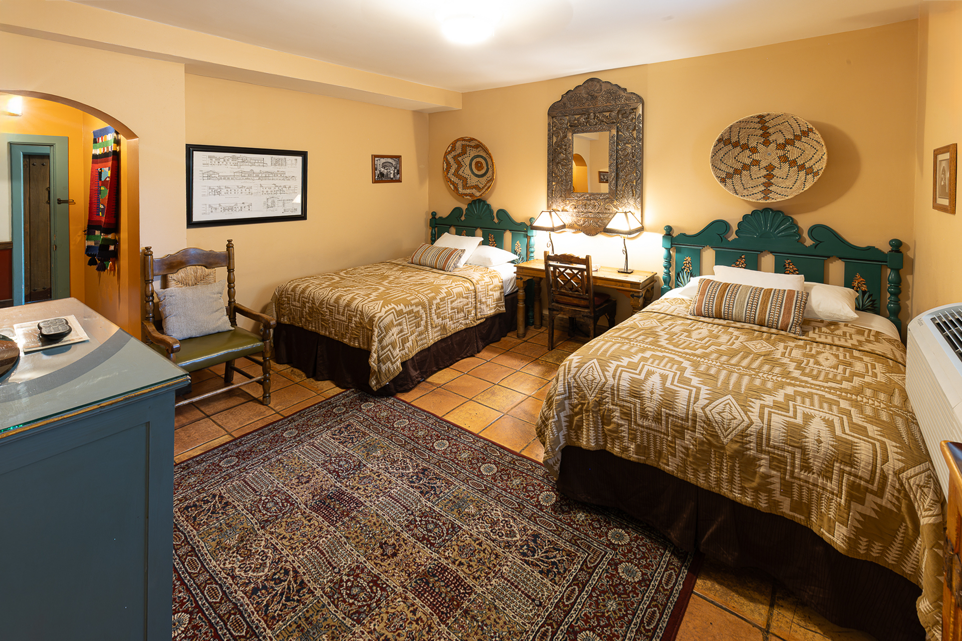 Two twin beds in a room with southwestern decor: teal headboards, patterned rugs, and warm-toned walls.