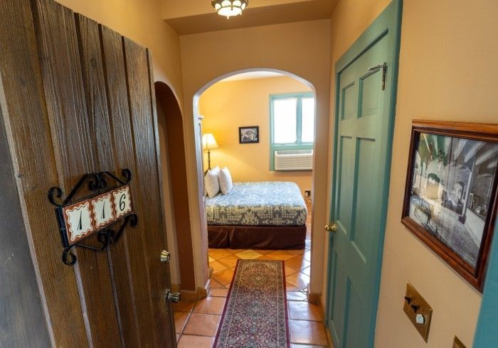 Entryway with arched doorway, leading to a bedroom. Features a wooden door, turquoise door, and patterned rug.