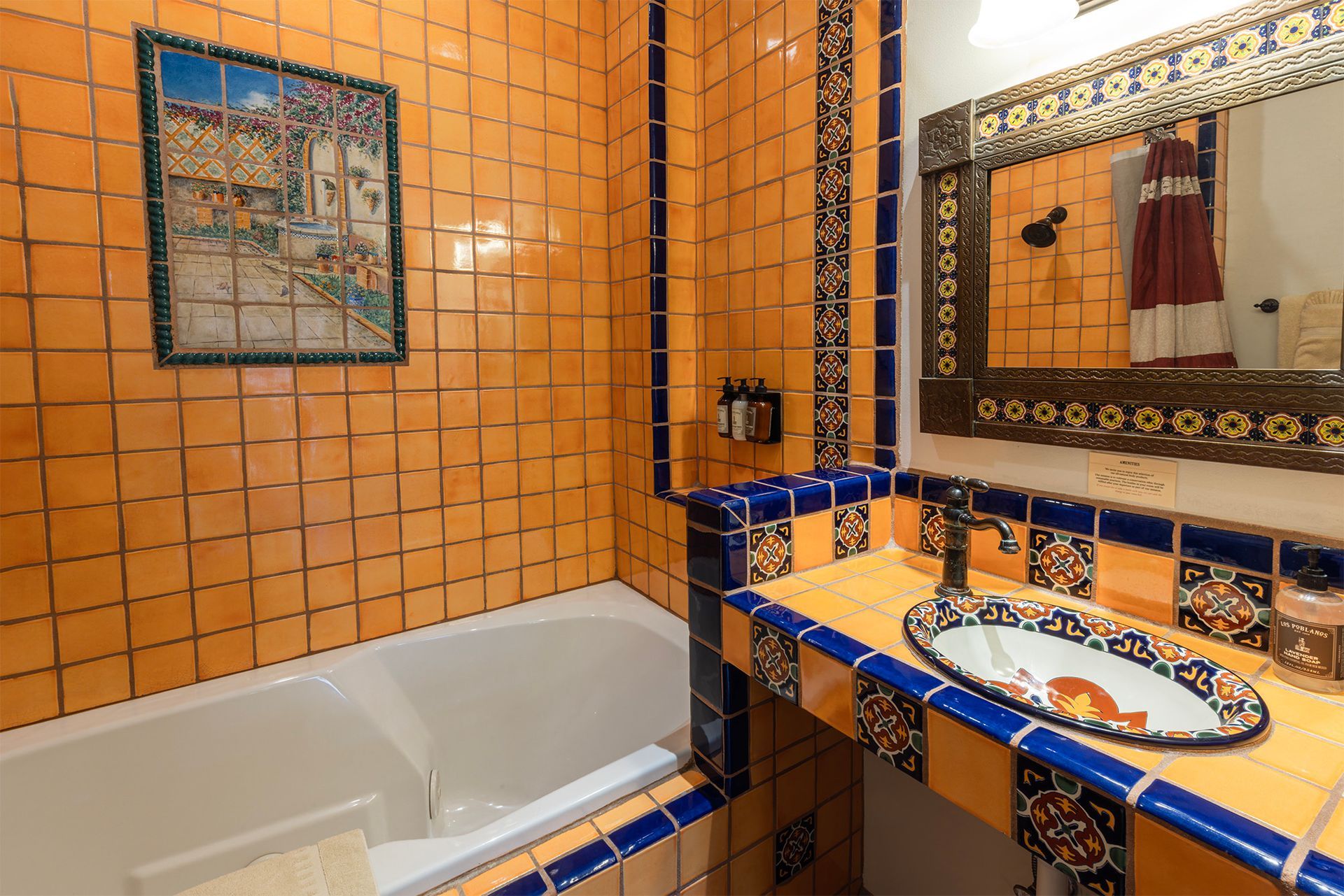 Bathroom with orange tiled walls and blue accents, sink, bathtub, mirror, and artwork.