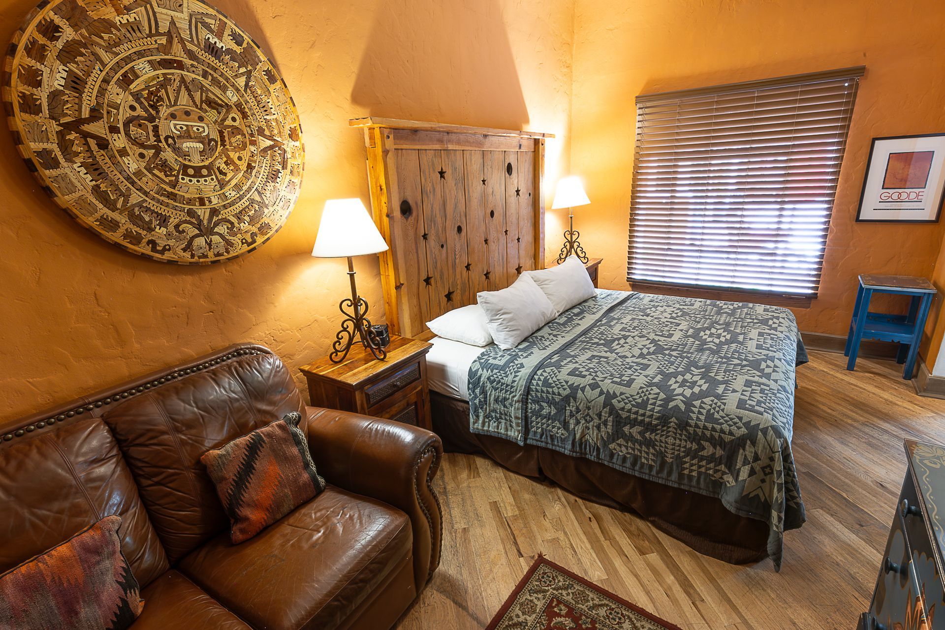 Southwest-style bedroom with leather couch, bed, woven wall decor, and orange walls.
