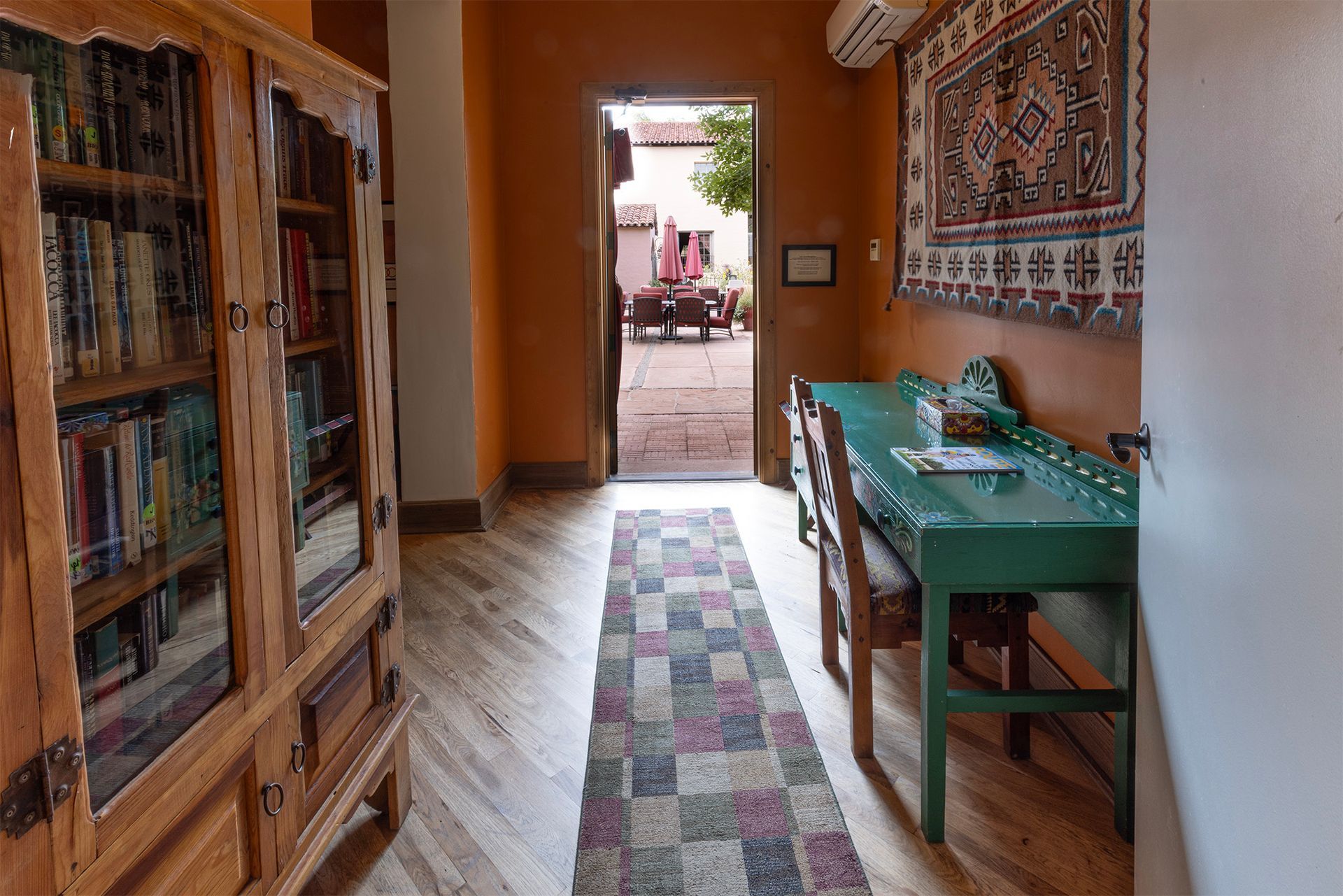 Hallway with bookcase, green desk, rug, and open doorway to courtyard.