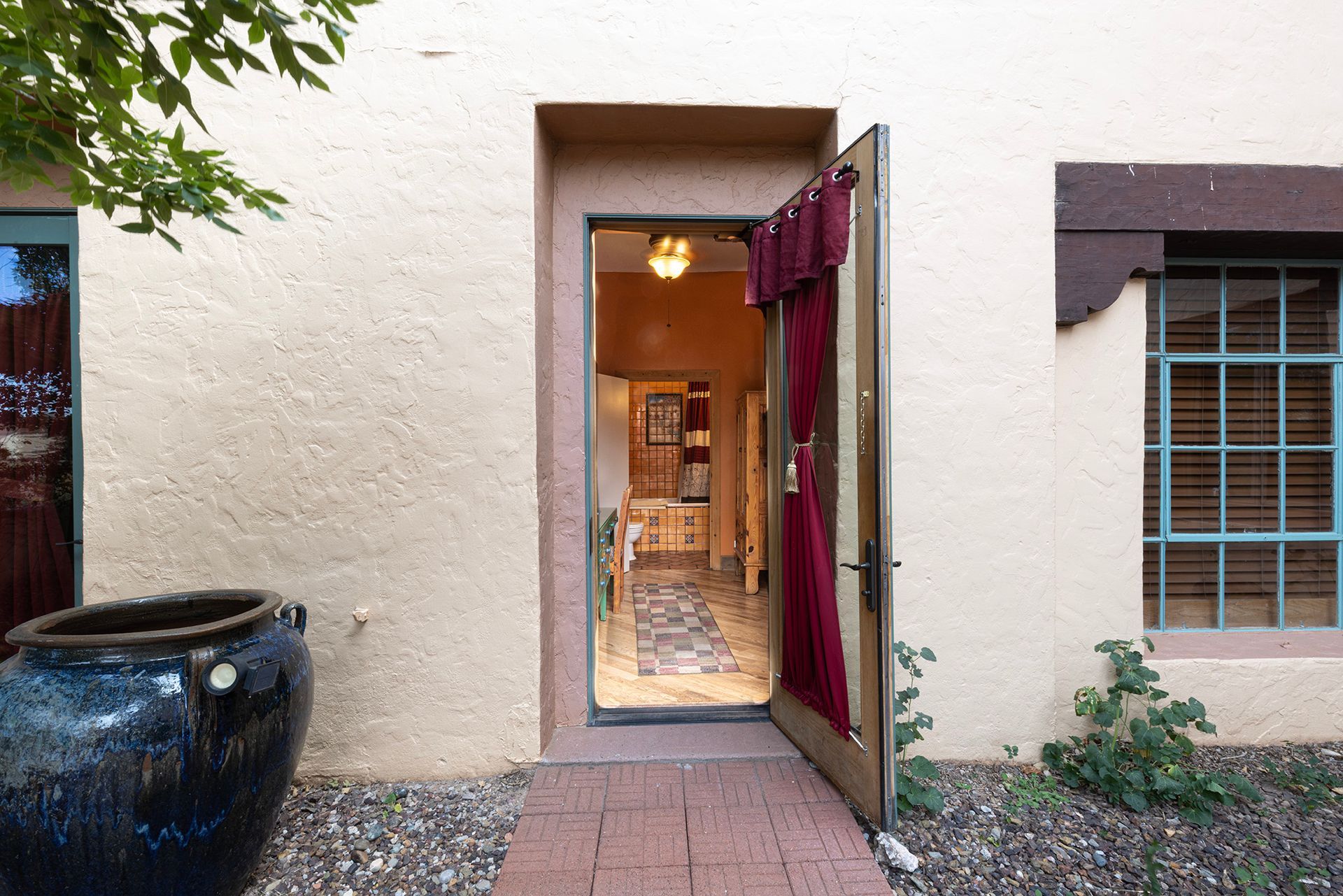 Open doorway of a light-colored building with a red curtain and a blue decorative pot.