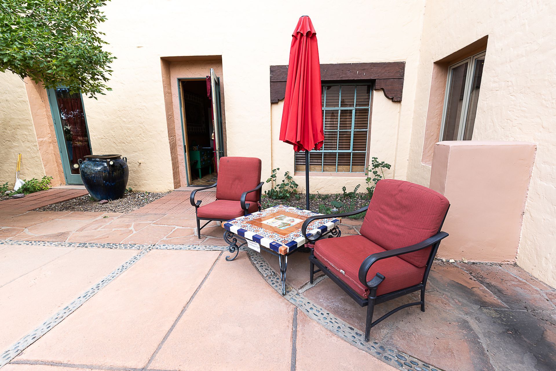 Courtyard seating area with two red chairs, table, and umbrella next to a light-colored stucco building.