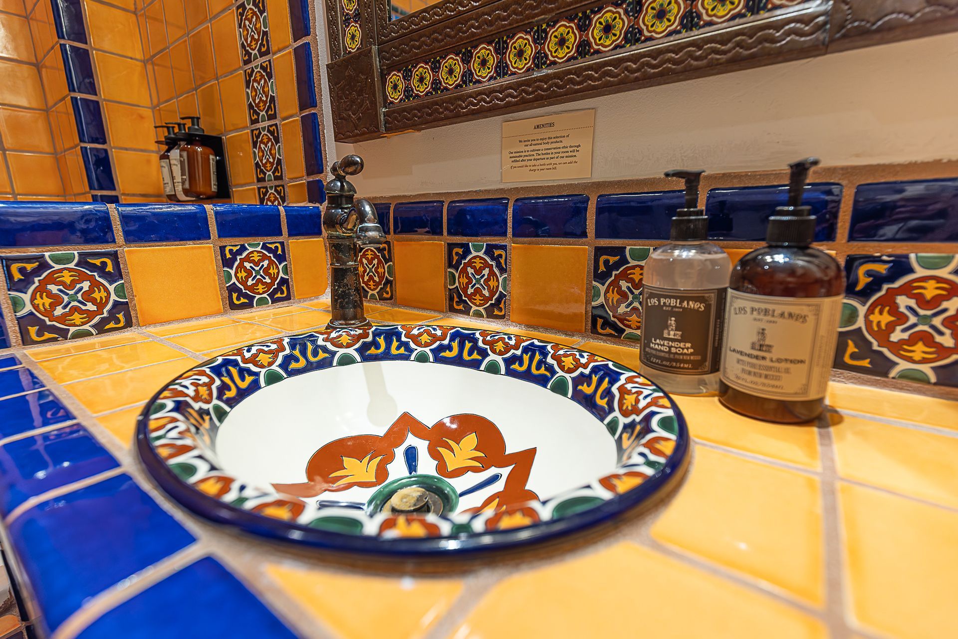 Colorful bathroom sink with patterned basin, surrounded by blue and yellow tile. Soap dispensers on the counter.
