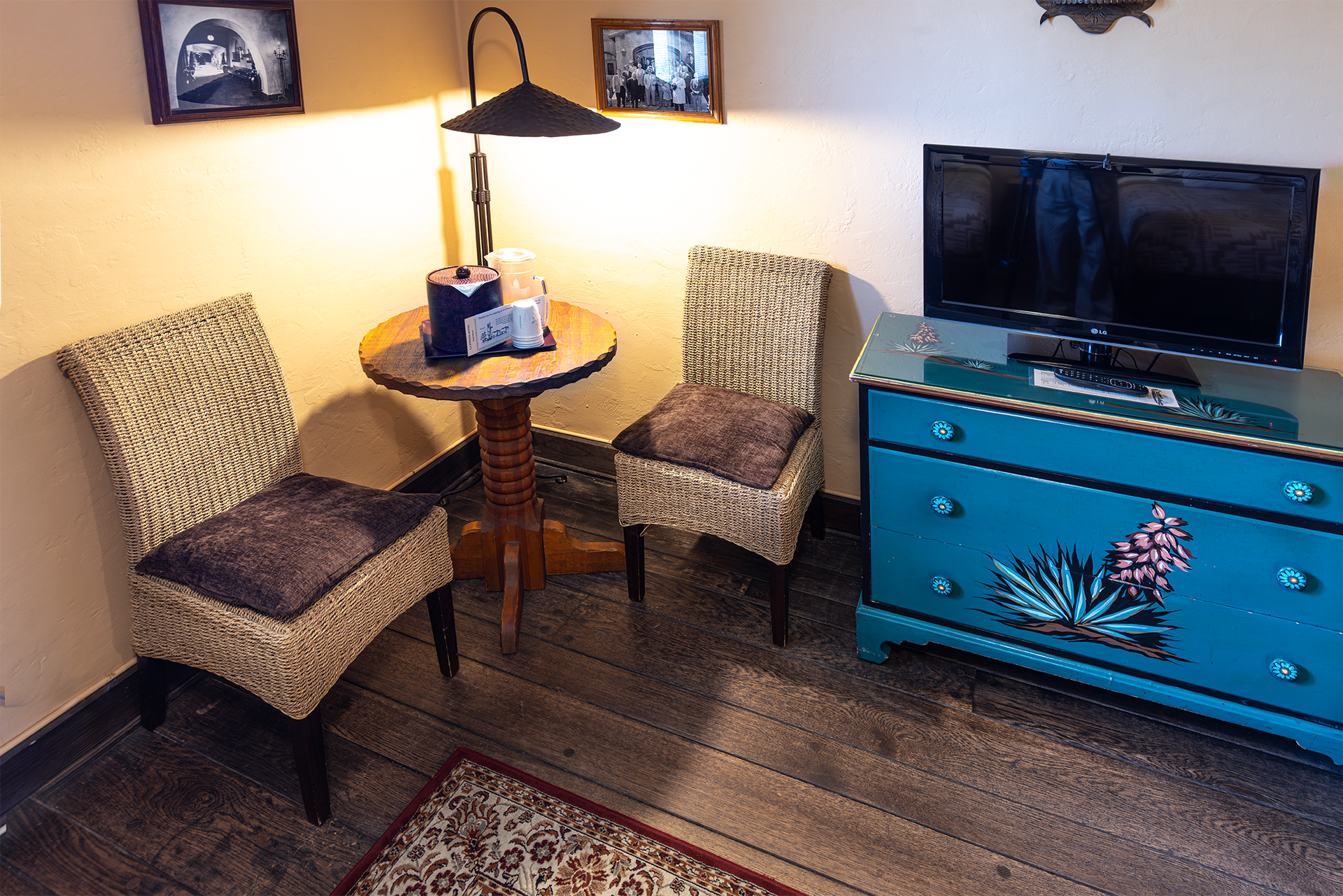 Two wicker chairs with purple cushions face a small table with a lamp in a room with a TV.