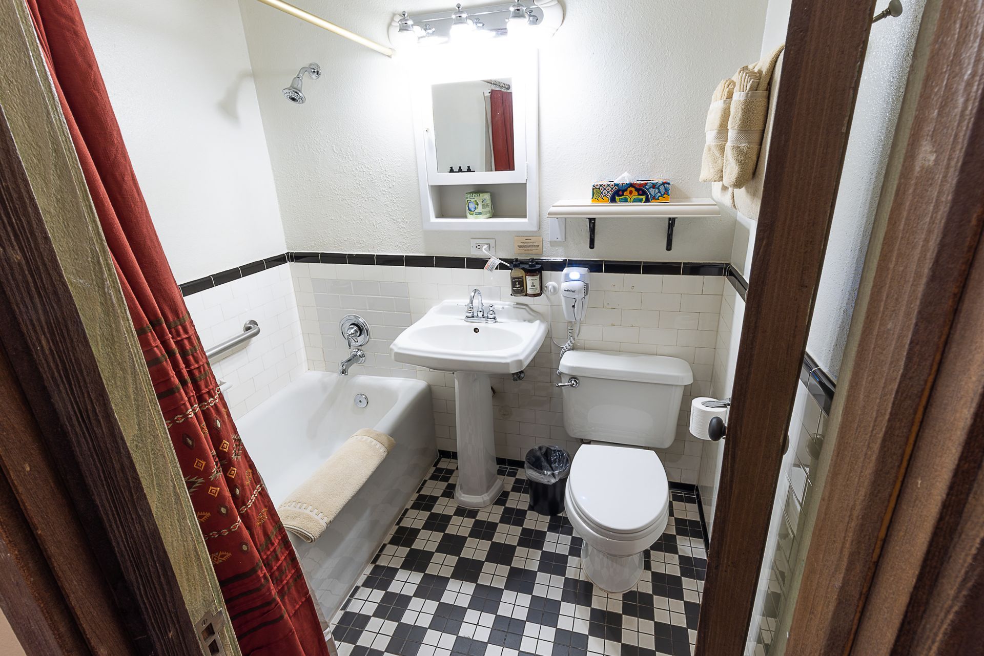 Small bathroom with checkered floor, white fixtures, and red shower curtain.