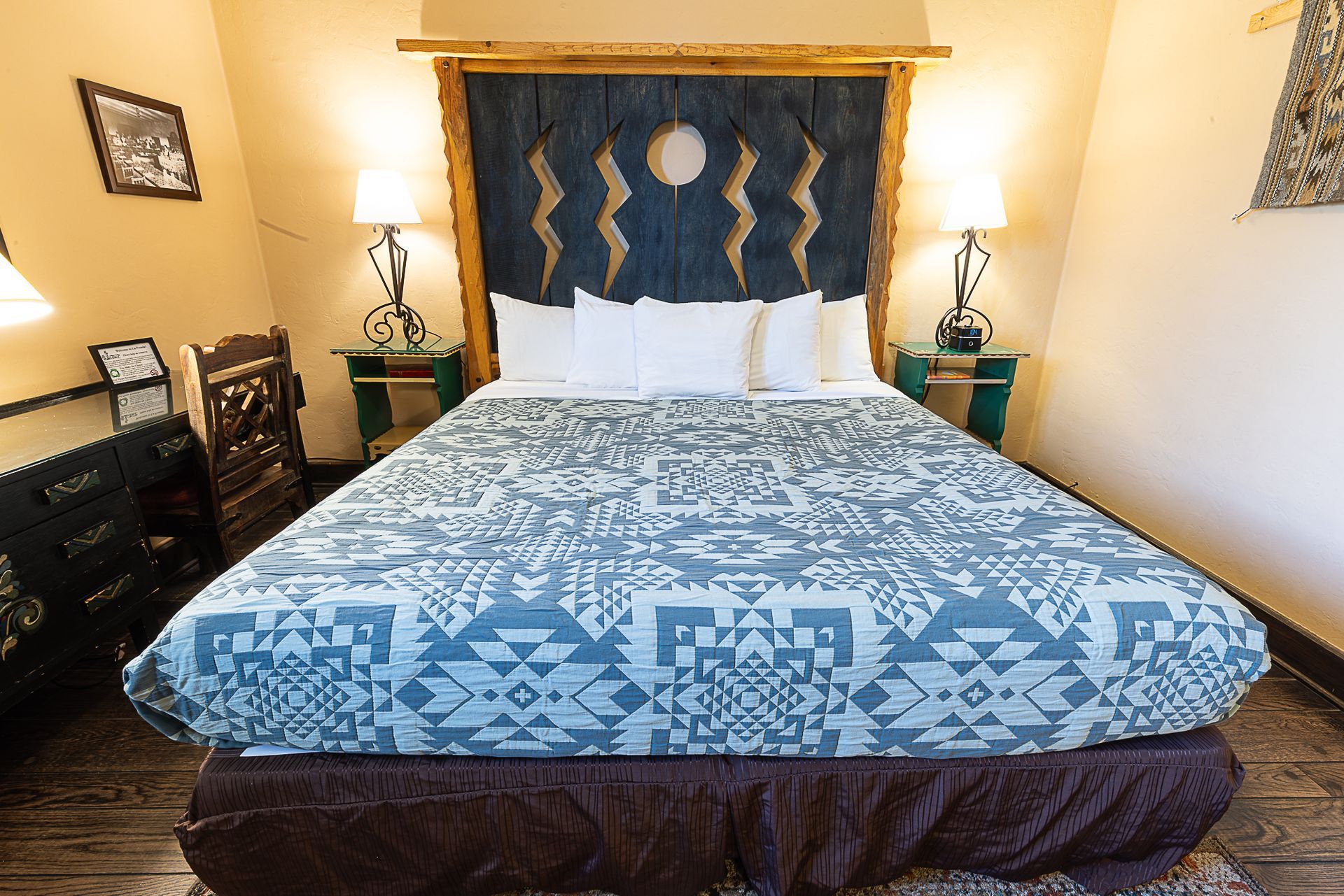 A hotel bedroom with a bed, wooden headboard with blue accents, and side tables with lamps.
