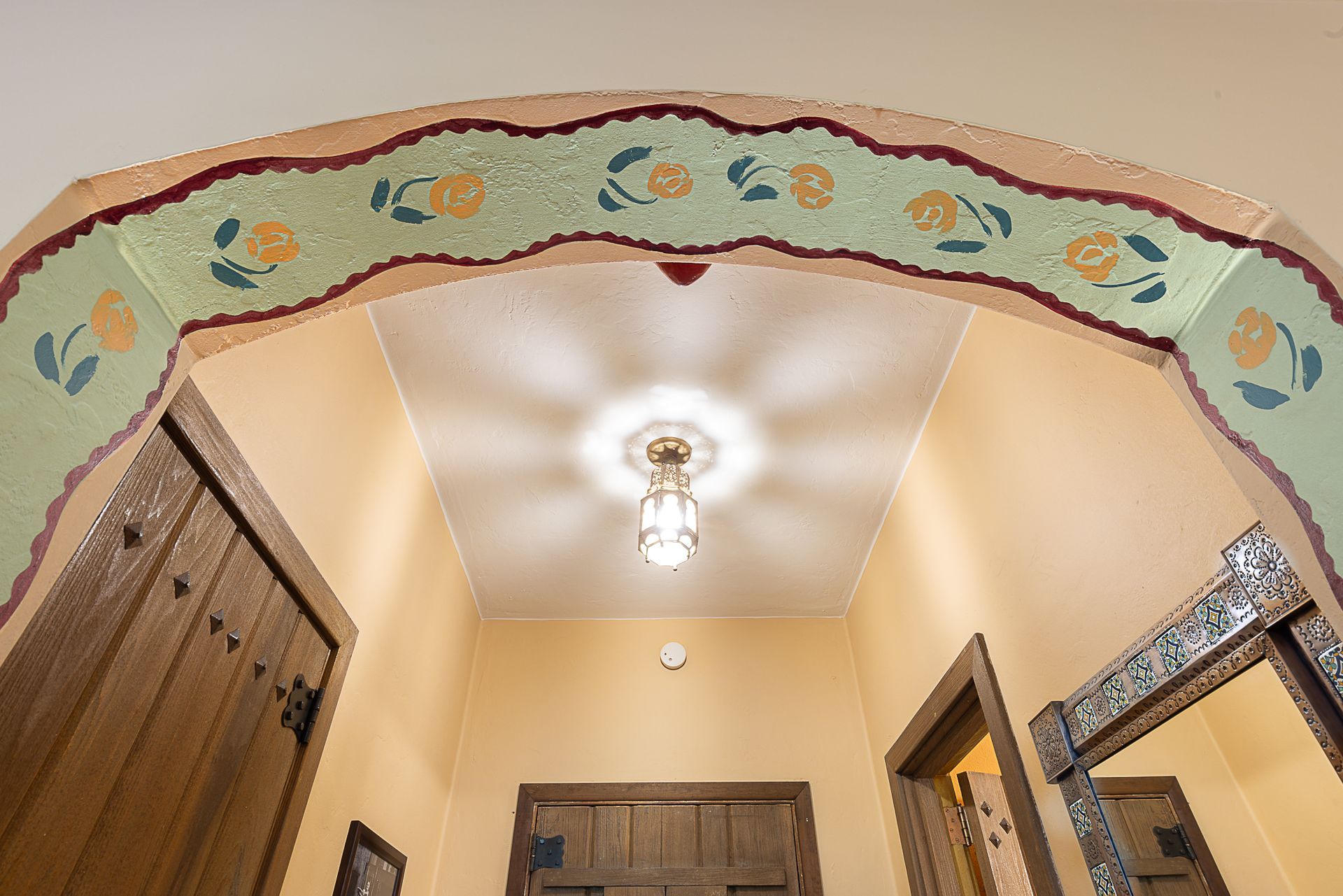 Interior hallway with arched doorway, floral painted trim, and ornate light fixture.