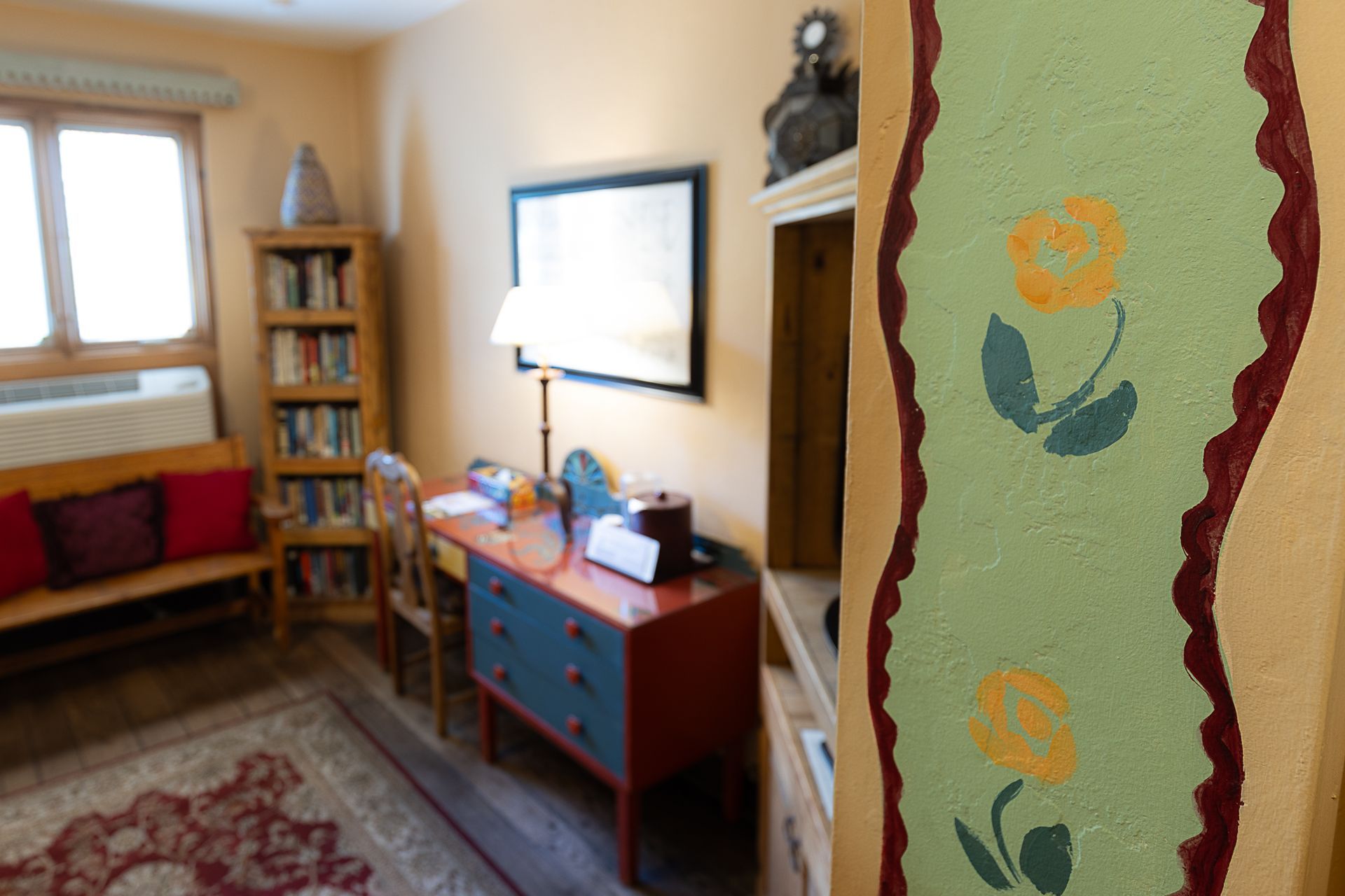 Room interior with desk, bookshelf, and floral painted wall detail.
