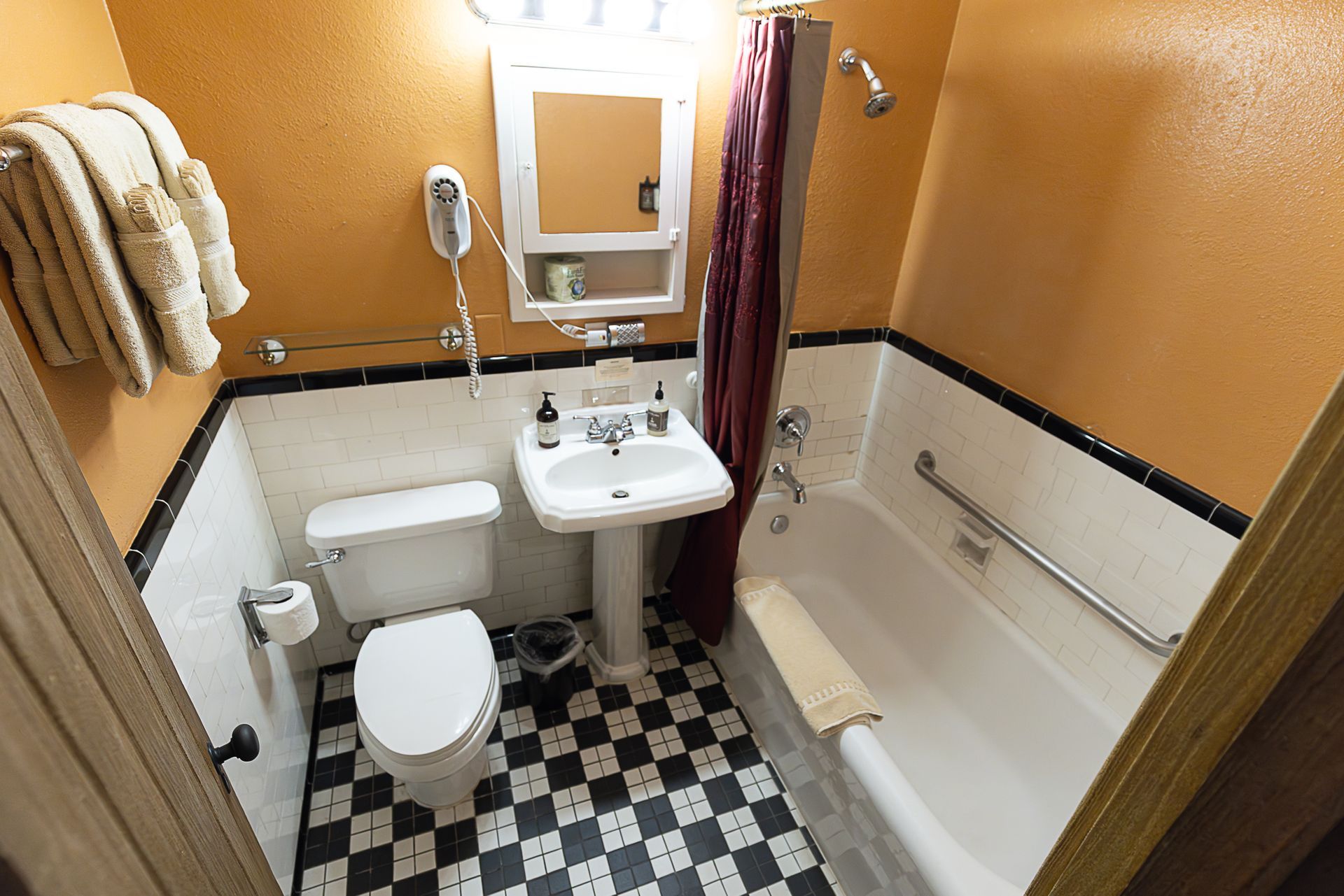 Small bathroom with a white toilet, pedestal sink, and bathtub. Black and white checkered floor.