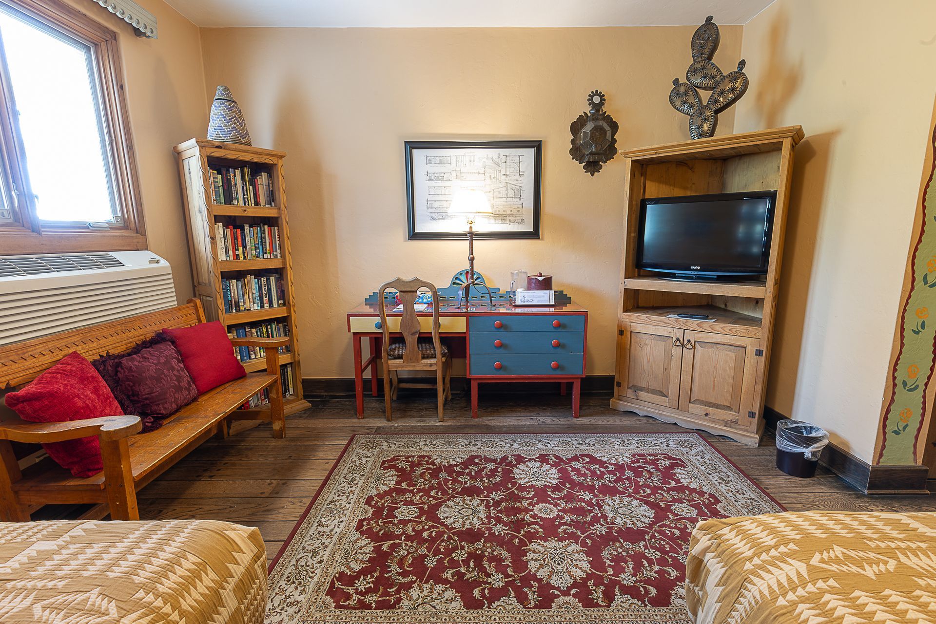 Cozy bedroom with bench, desk, bookshelf, TV stand, and patterned rug on wooden floor.