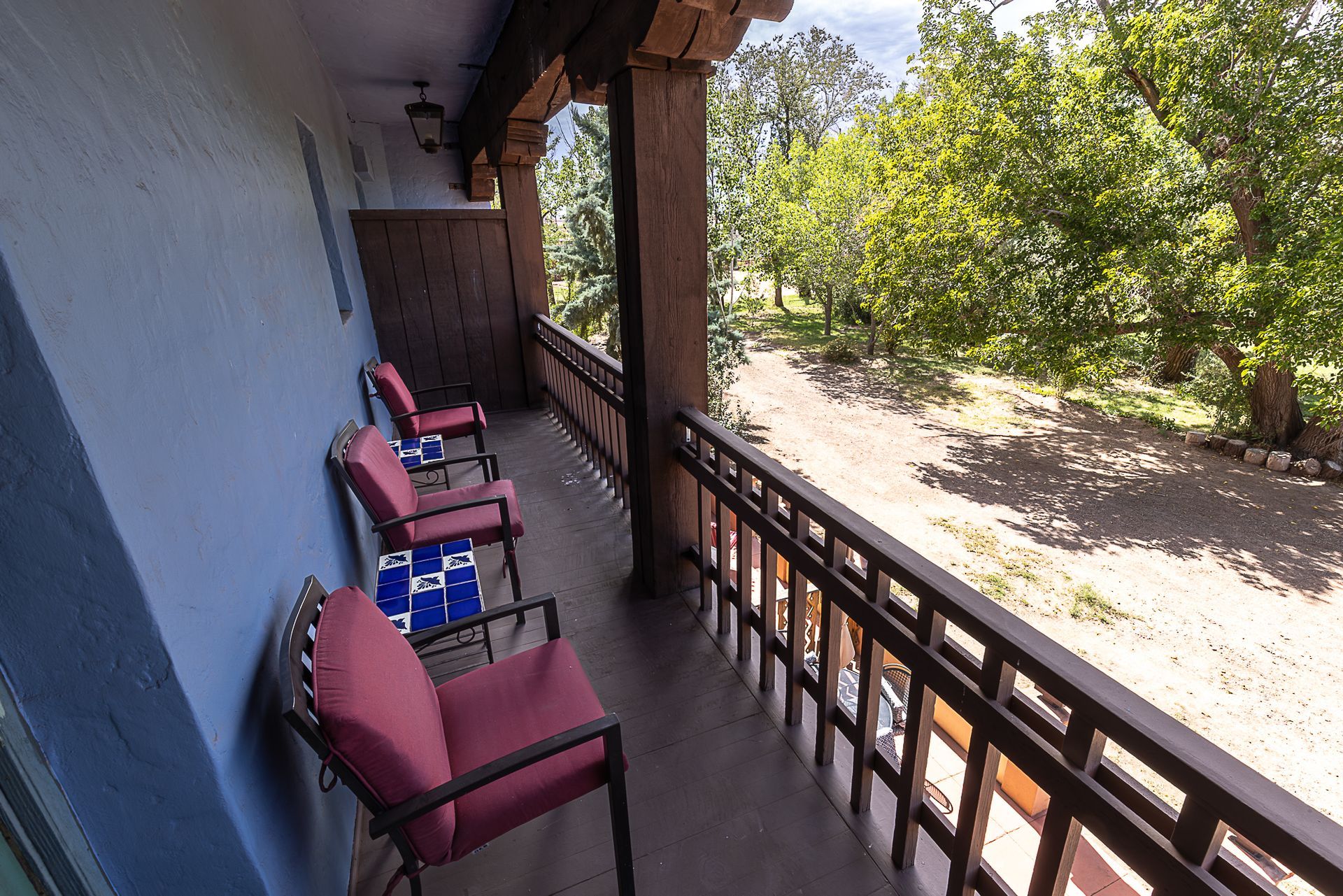 Balcony with red chairs overlooking a dirt path and trees.