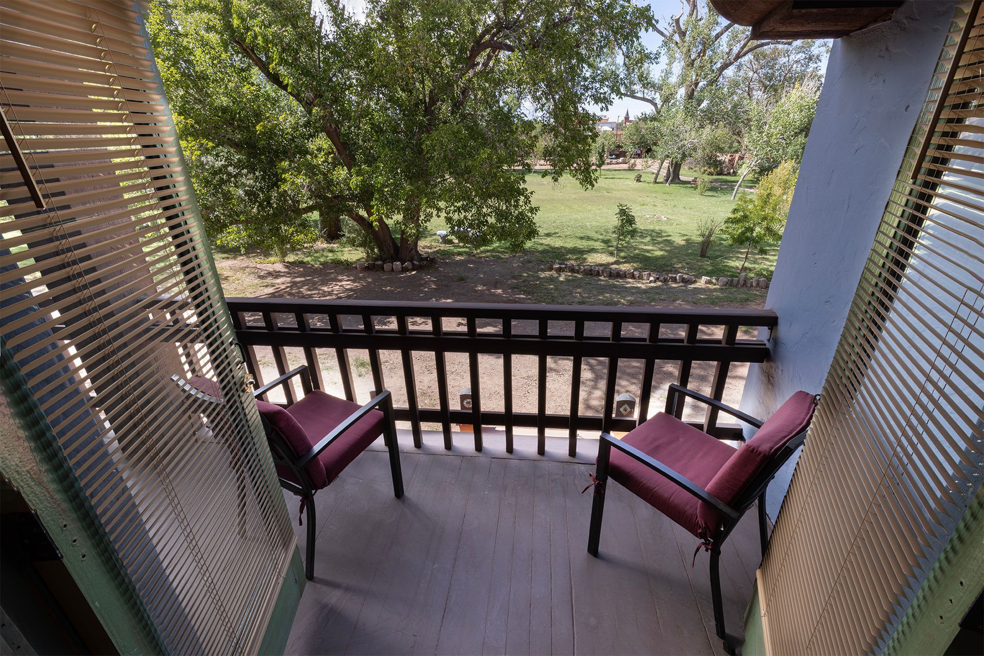 Two red chairs on a balcony overlooking a grassy yard, framed by woven screens and a wooden railing.