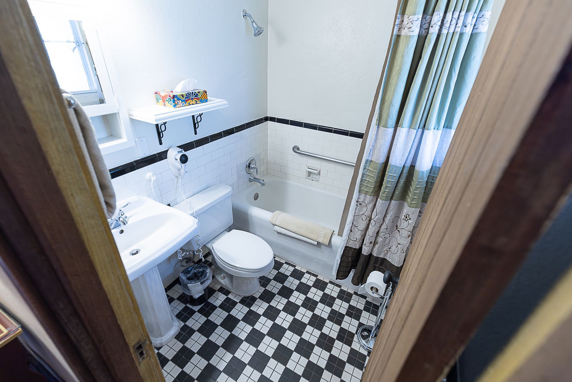 Small bathroom with black and white checkered floor, white fixtures, and floral shower curtain.