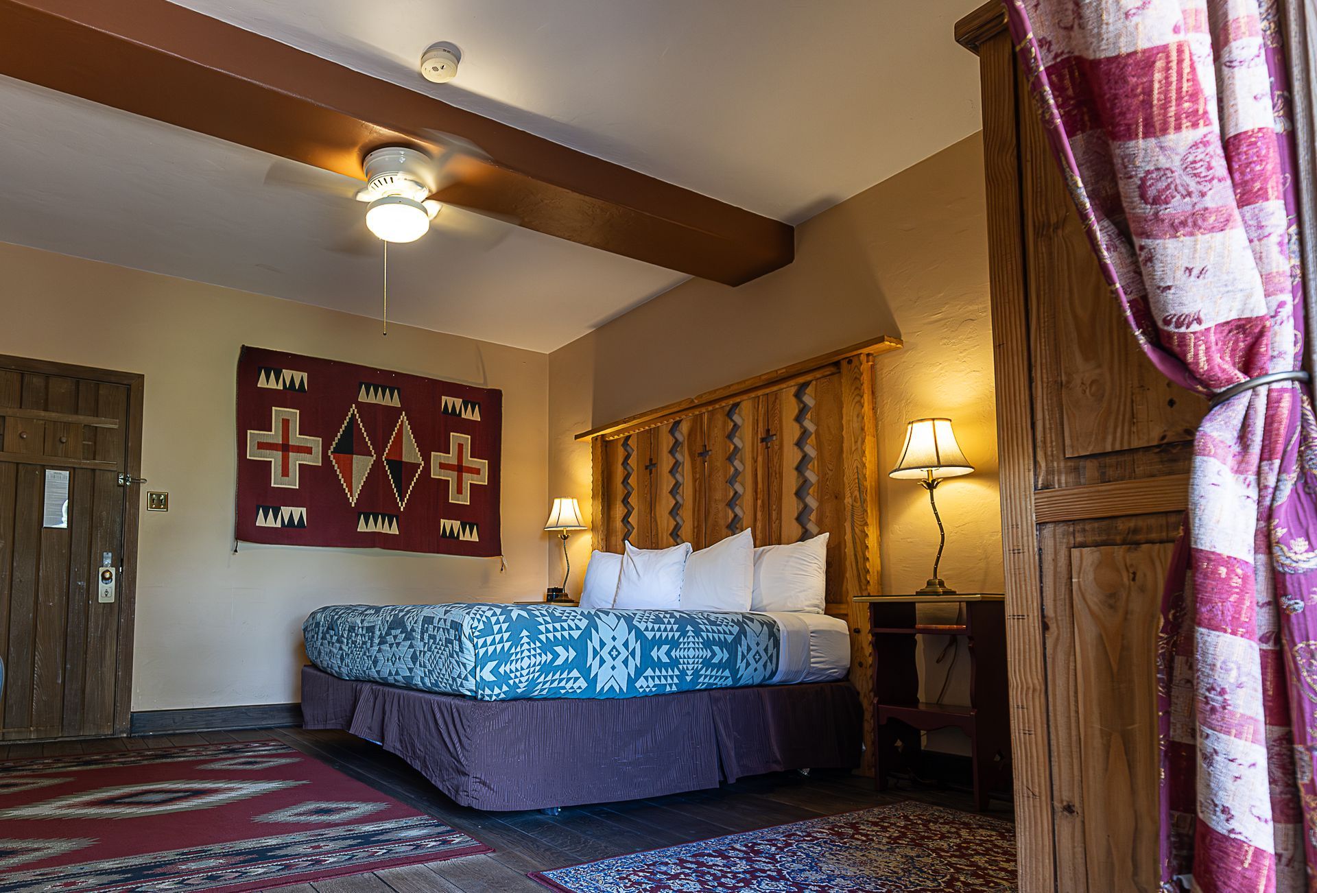 Southwestern style hotel room with queen bed, patterned rug, and a wood headboard.