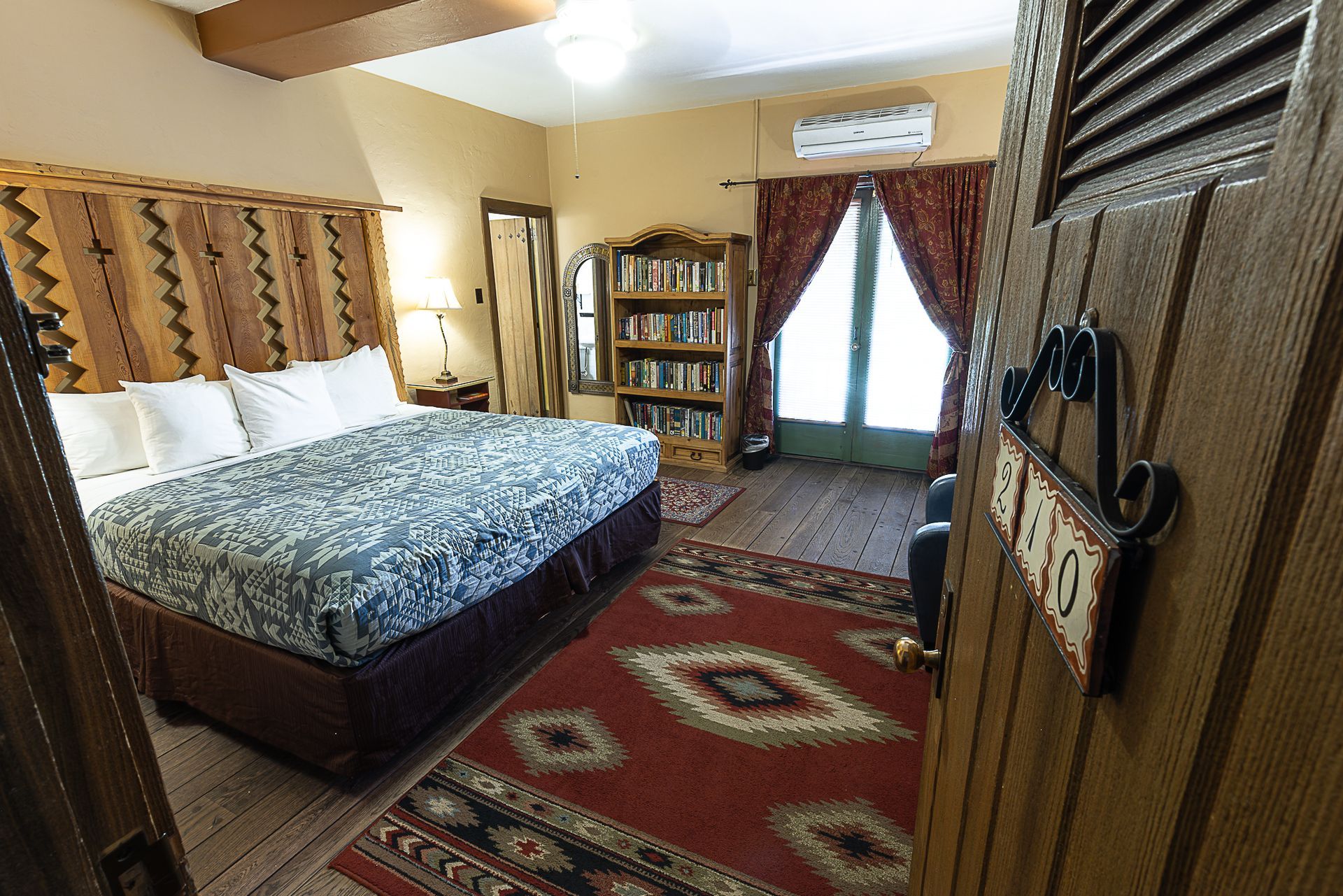 Hotel room interior with king bed, patterned rug, and door to outside.