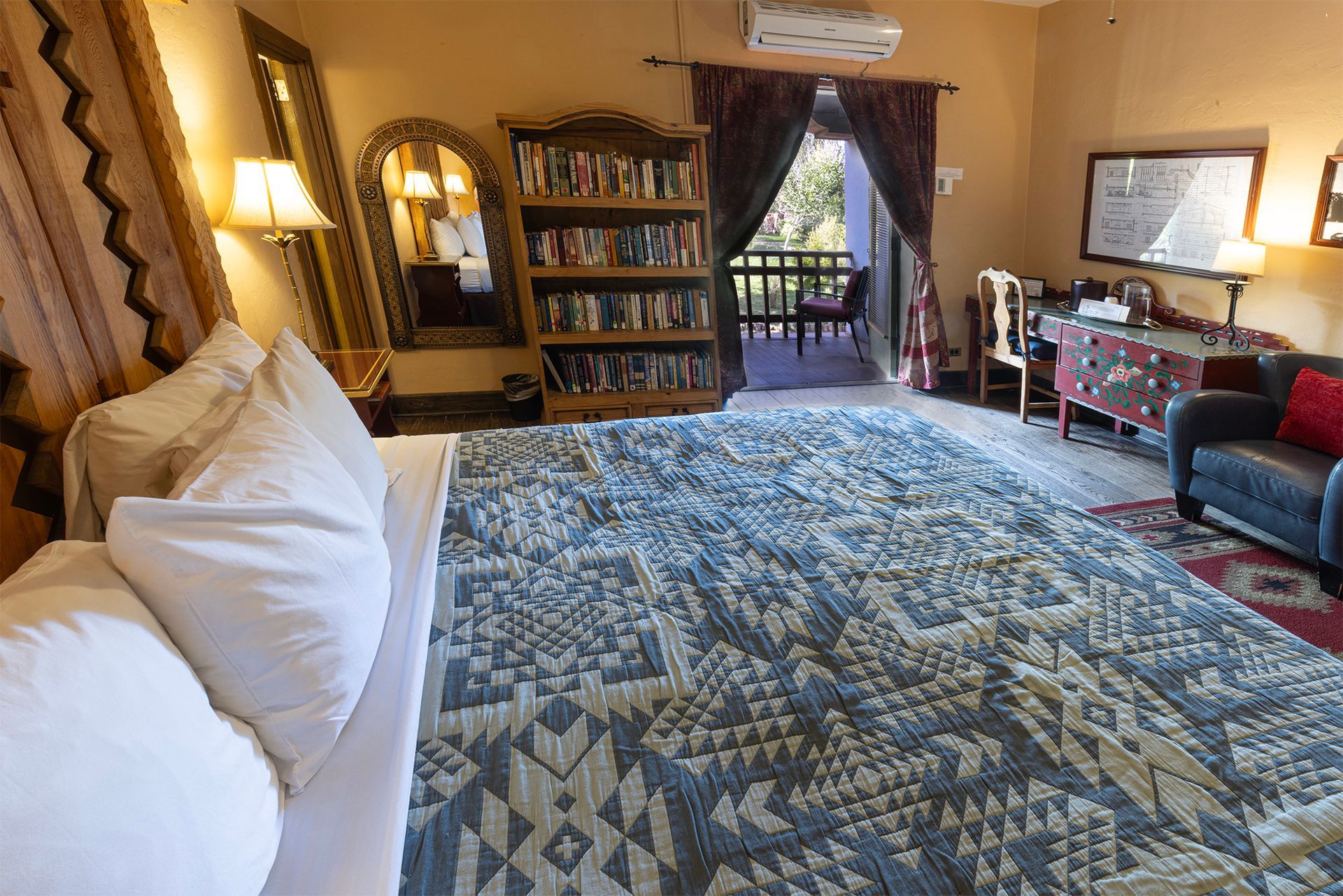 Bedroom with king bed, bookshelf, balcony, and seating area.