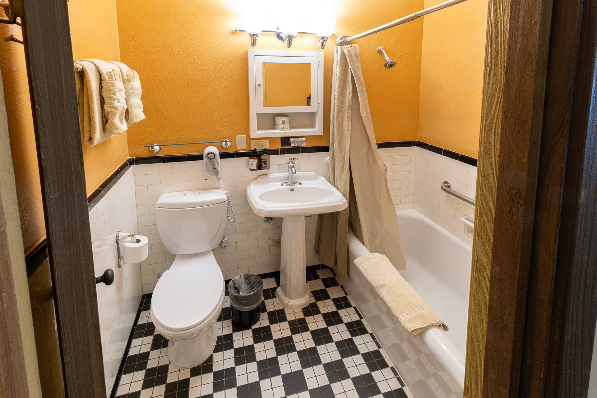 Bathroom with checkered floor, white fixtures, orange walls, and a shower curtain.