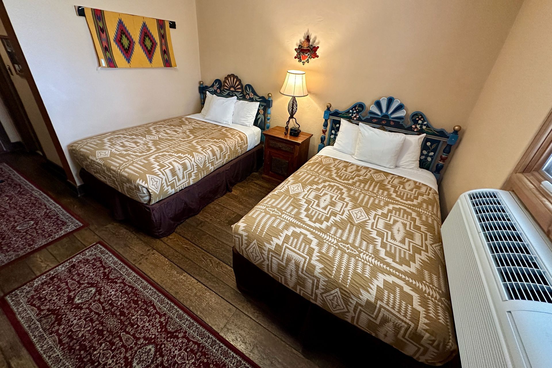 Two twin beds in a room; golden patterned bedspreads, colorful headboards, and rug.