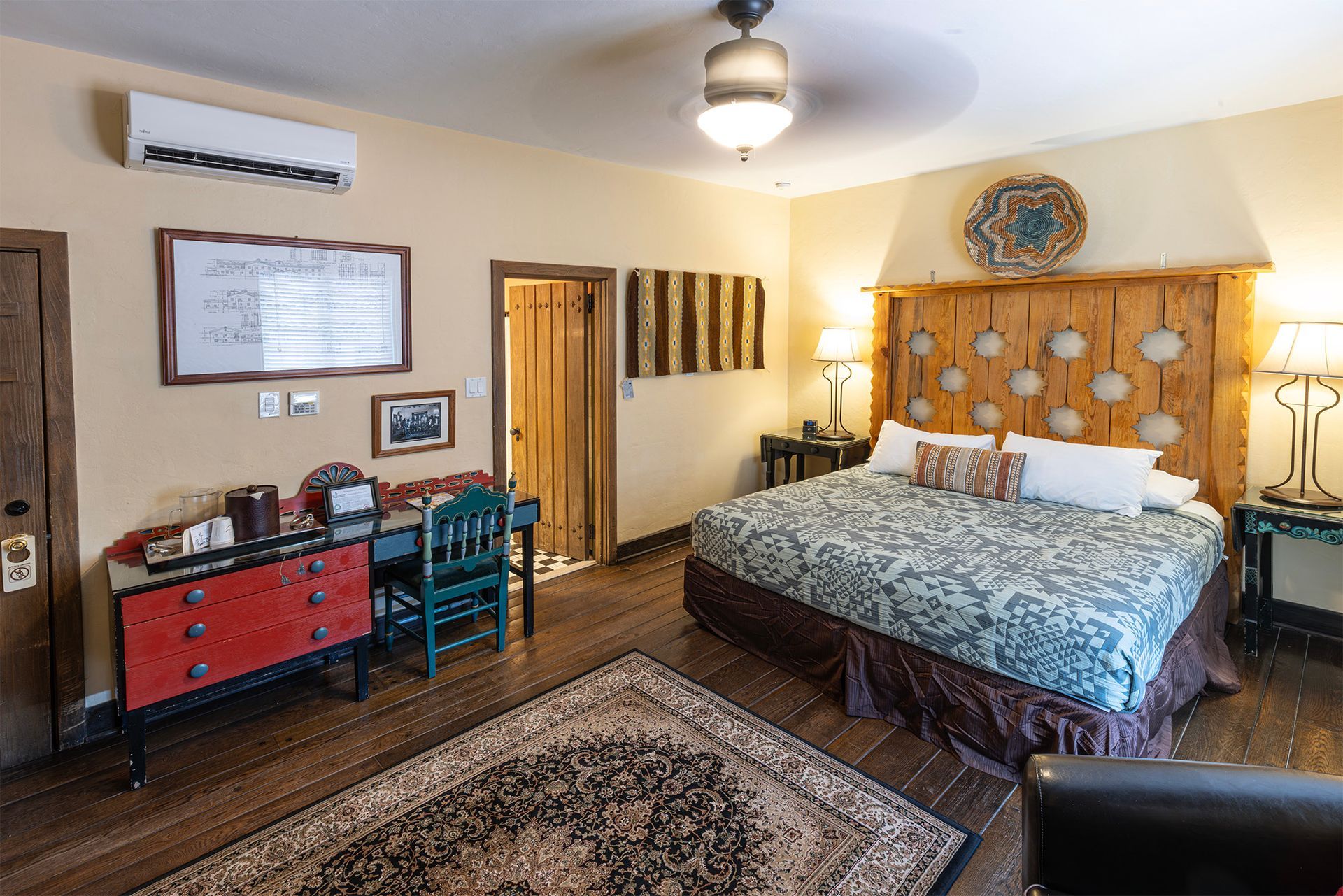Bedroom with wooden headboard, desk with red dresser, and area rug.