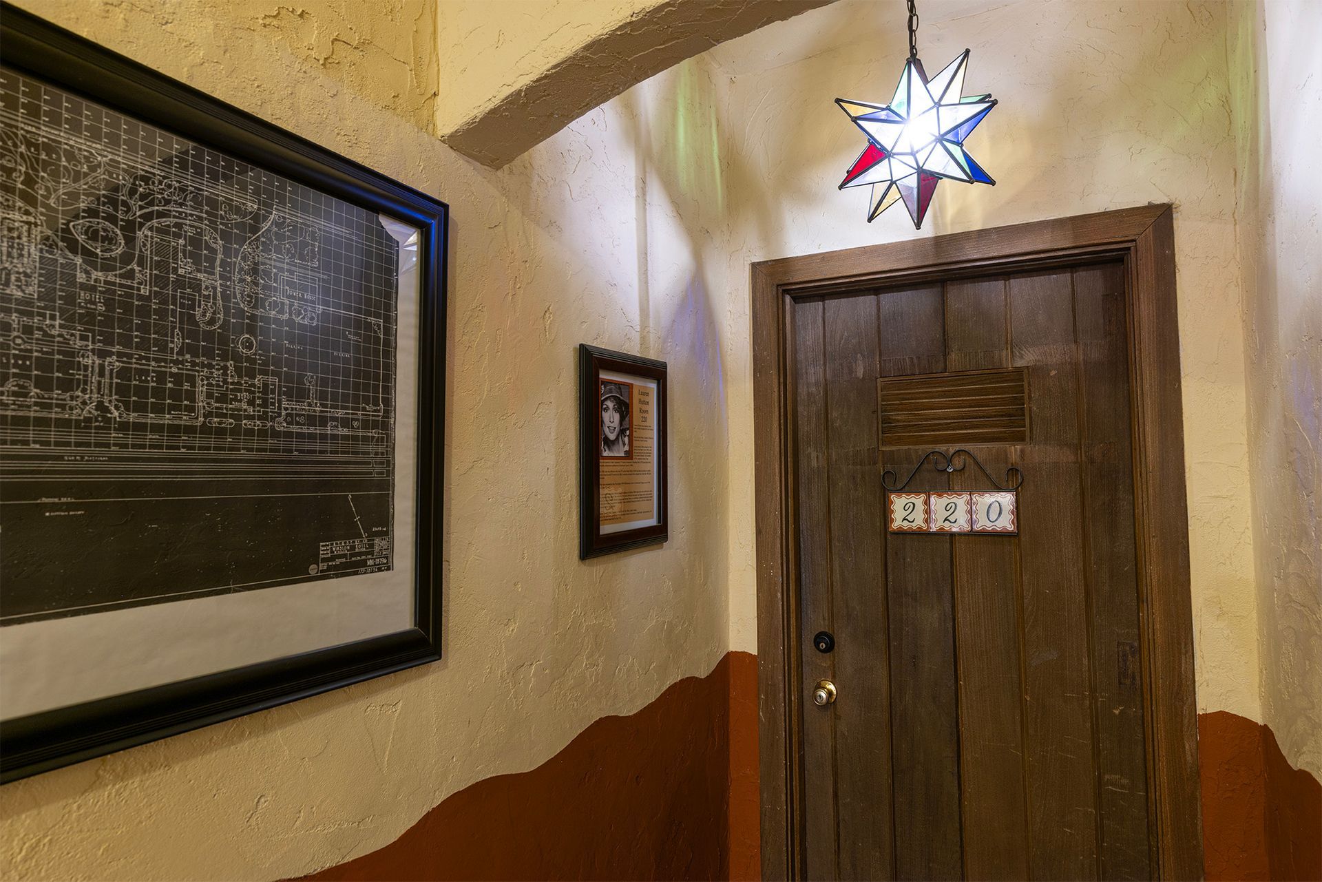 Narrow hallway with wood door, artwork, and star-shaped hanging light. Brown and beige walls.