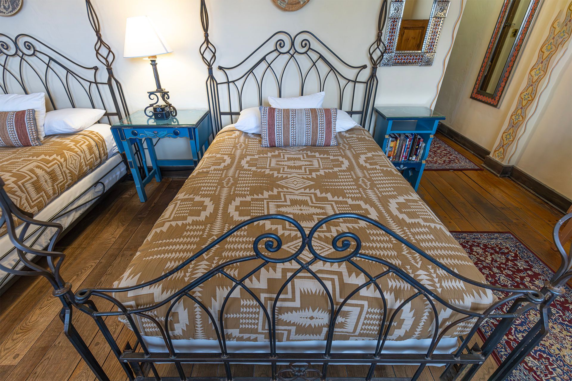 Two twin beds with patterned blankets and decorative metal headboards, in a room with wood floors.