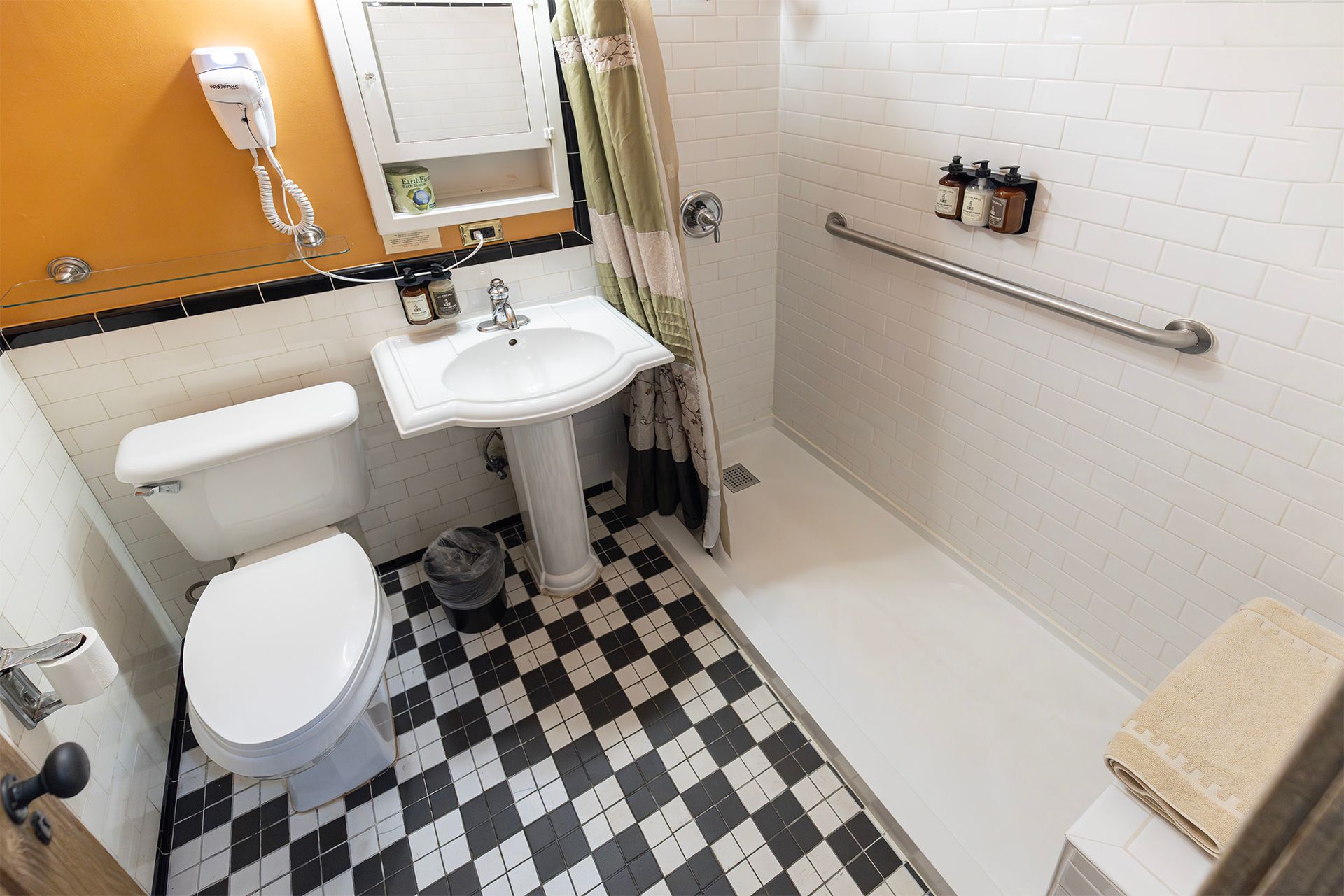Bathroom with pedestal sink, toilet, and shower with grab bar. Black and white checkered floor.