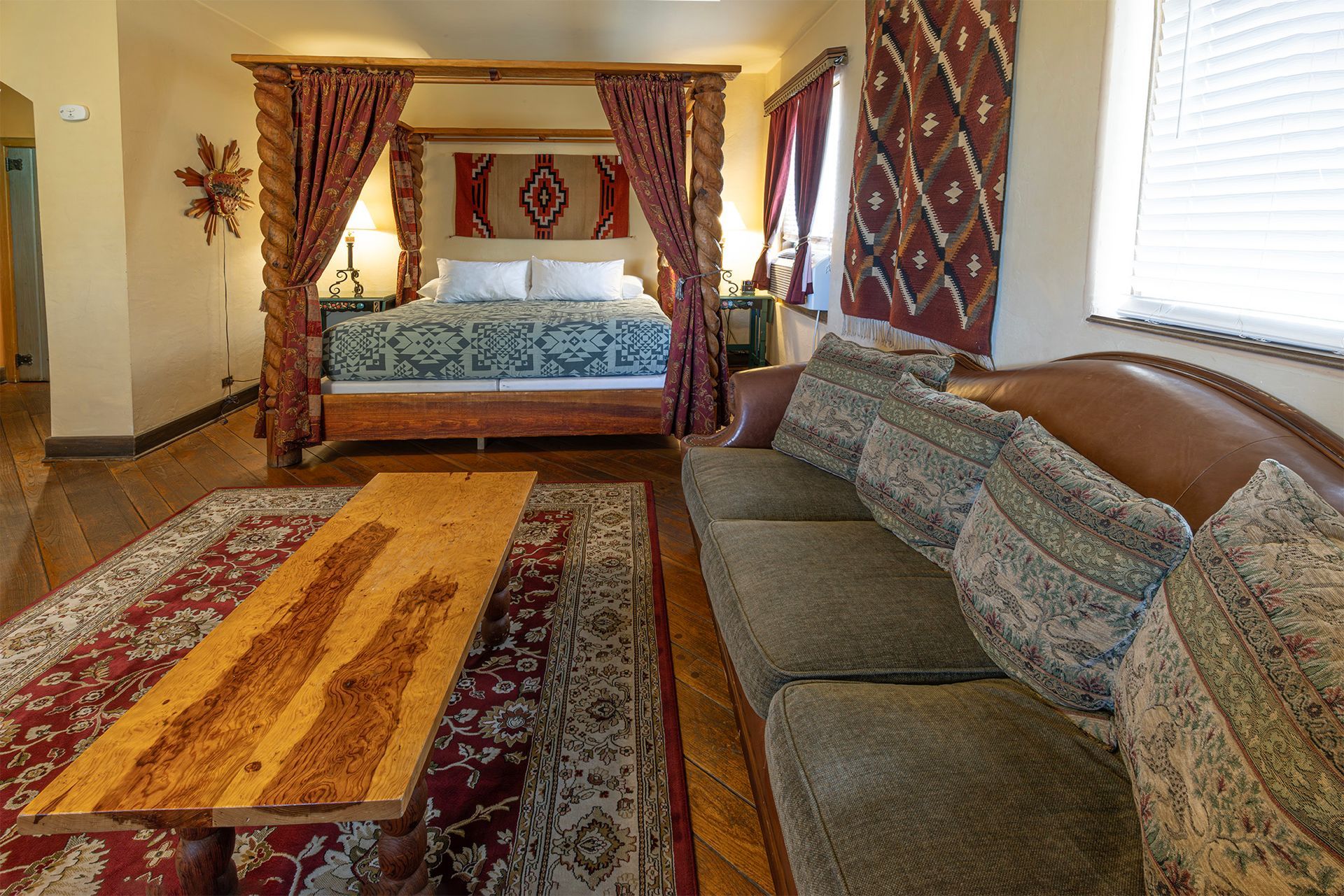 Bedroom with a four-poster bed, a sofa, a wooden table, and southwestern-style rugs and decor.
