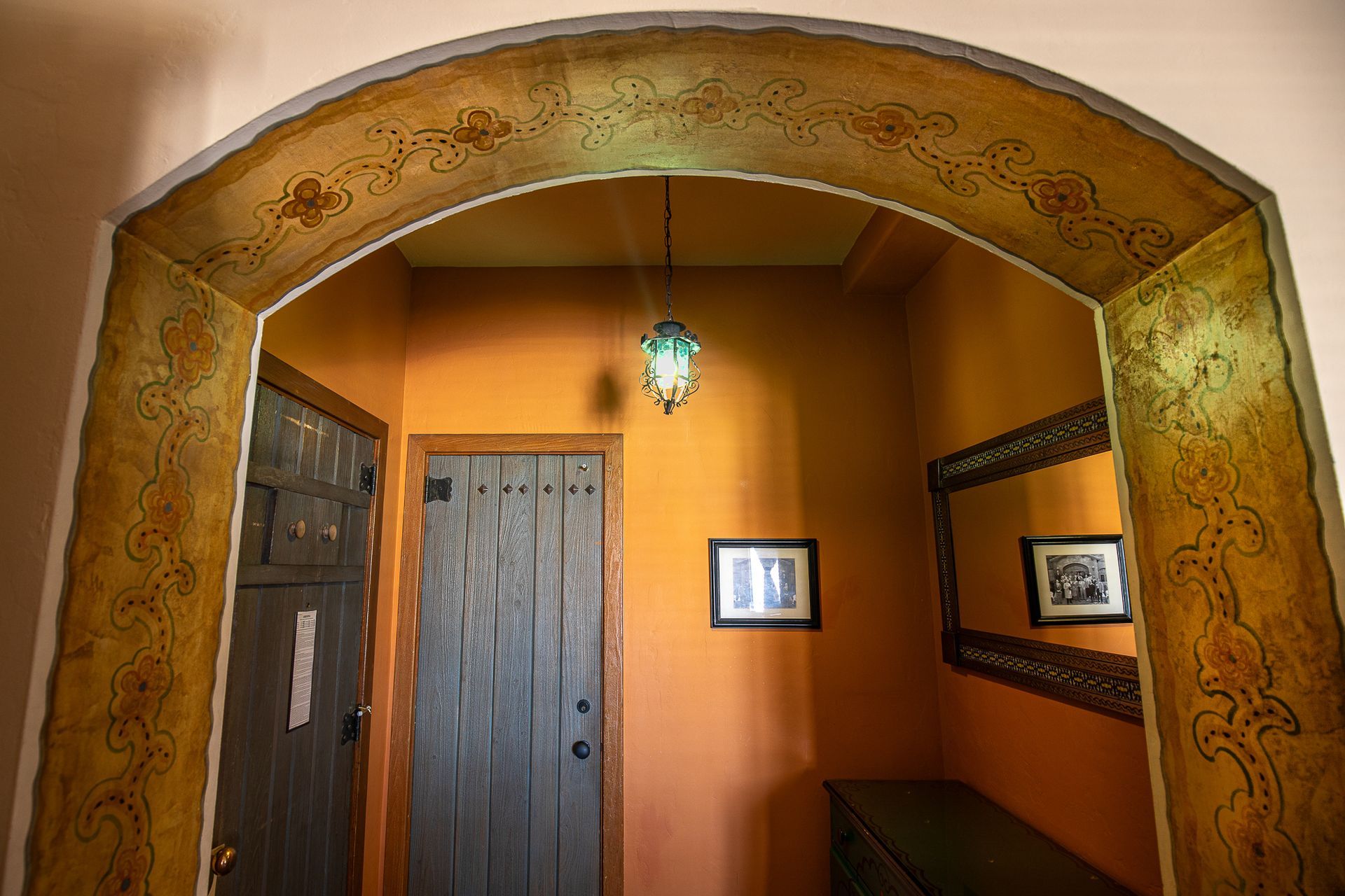Entryway with arched opening, gold trim, and orange walls, featuring wood doors, mirror, and hanging light.