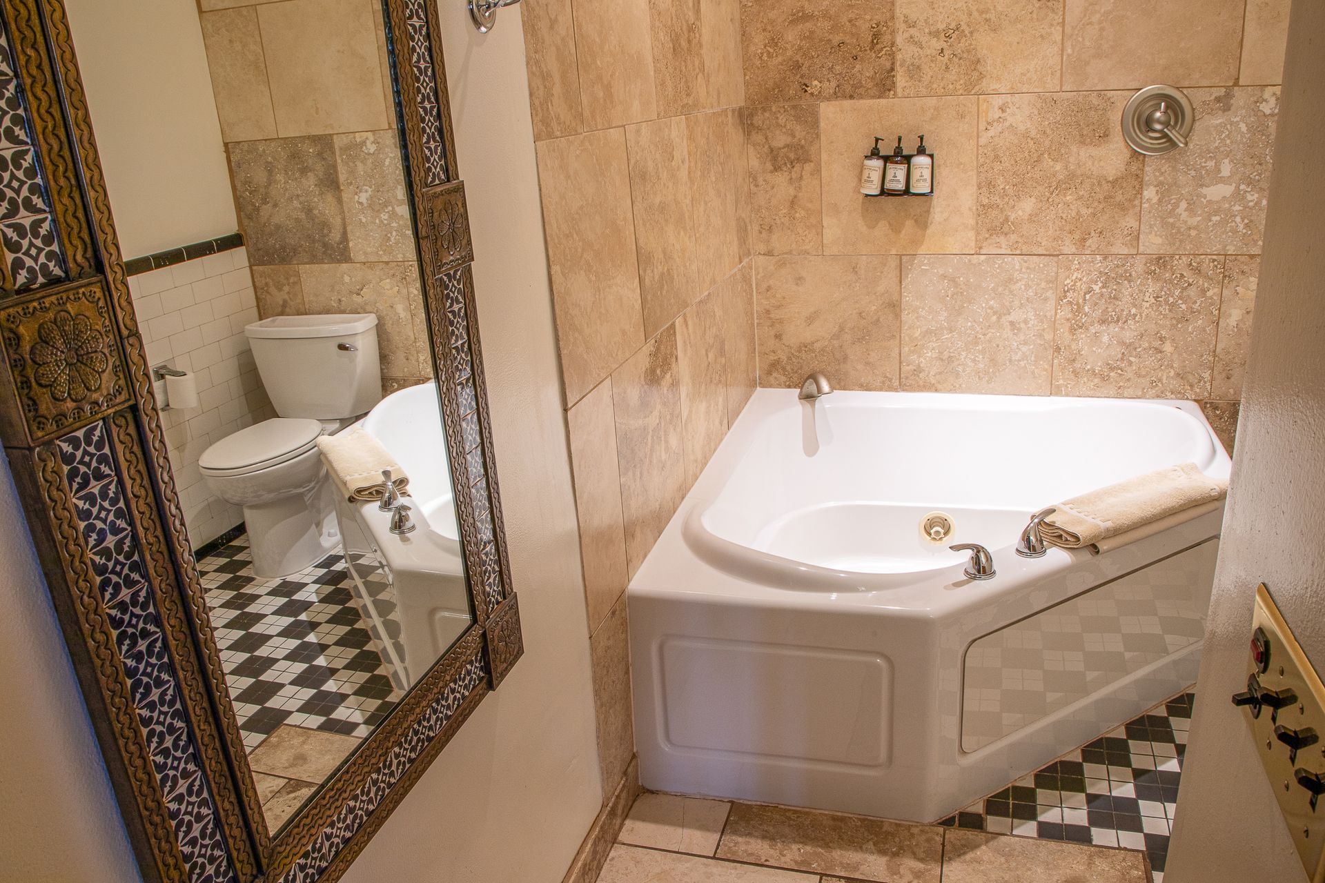 Bathroom with corner tub, toilet, checkered floor, beige tile walls, and mirror.