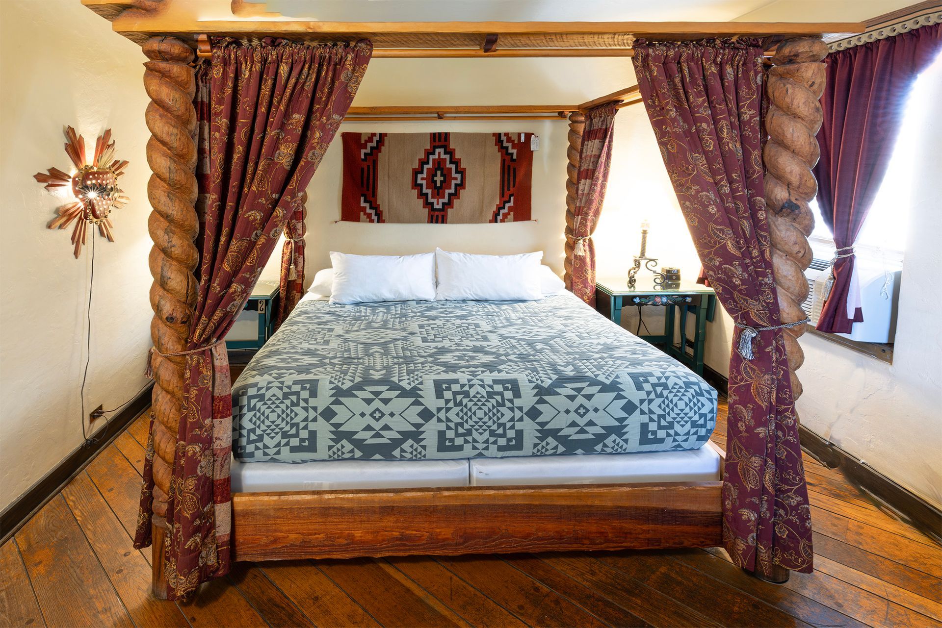 Bedroom with canopy bed, draped in red curtains, turquoise and white quilt, rug on wall.