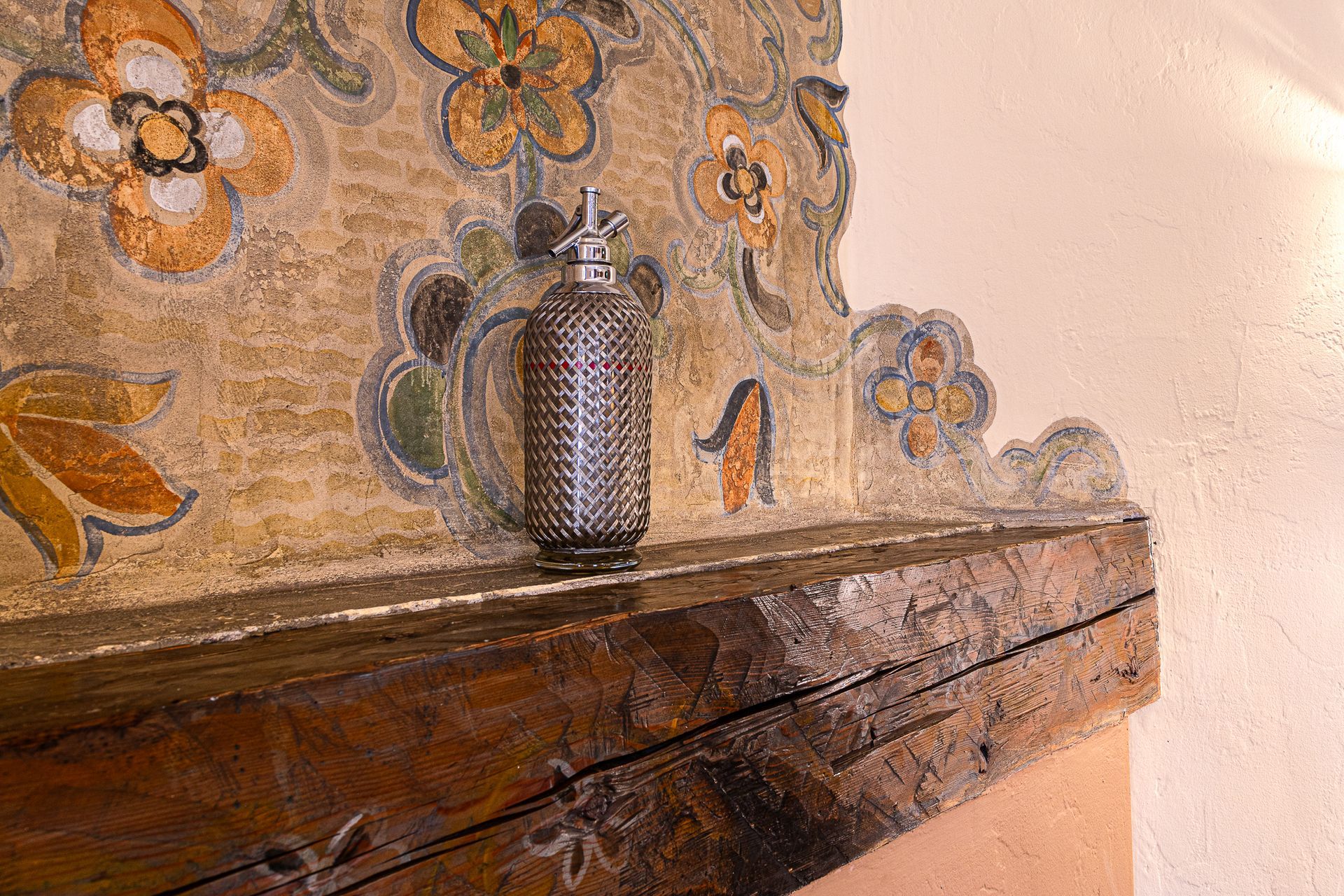 Dark glass bottle on a weathered wooden beam with painted floral background.