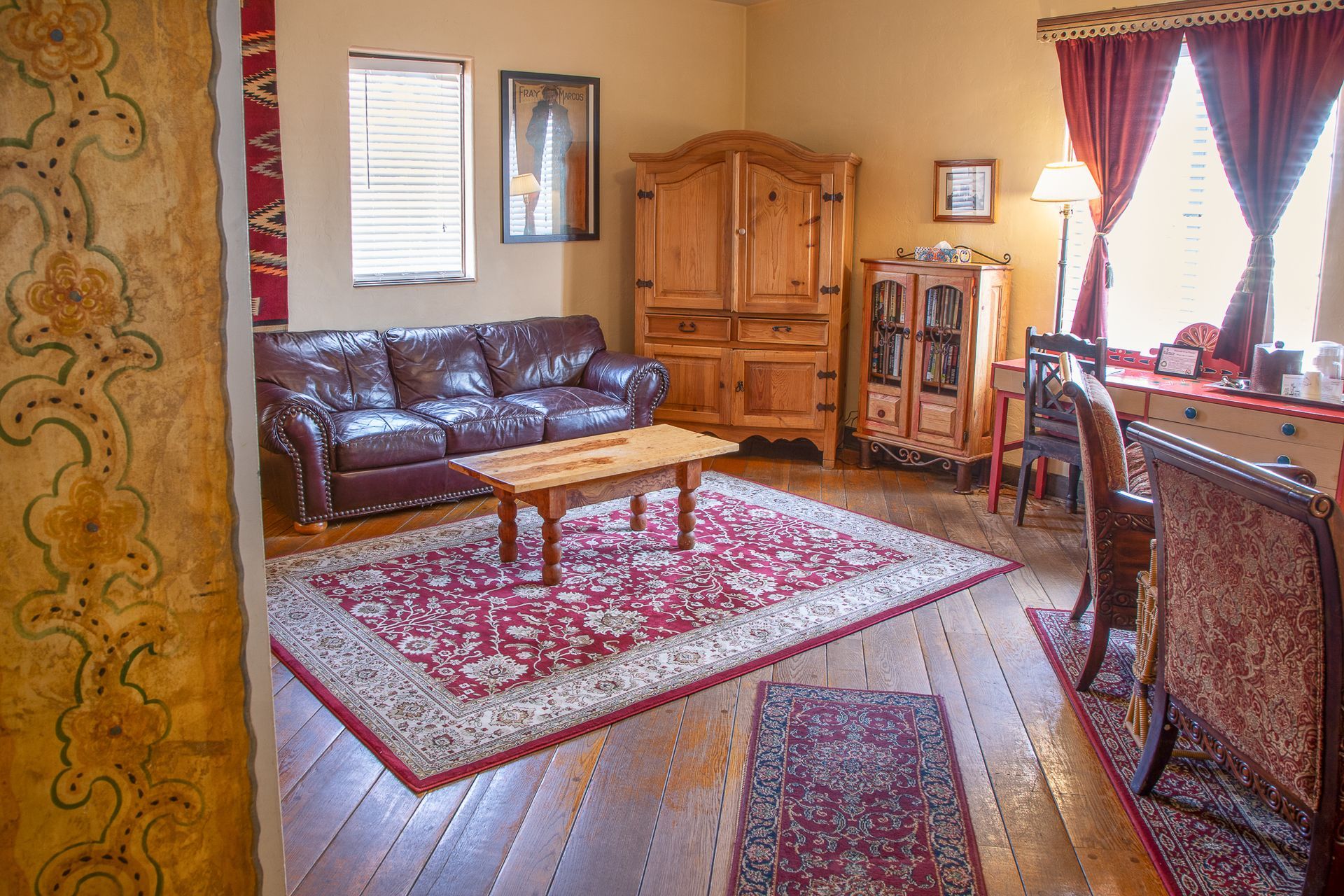 Cozy room with leather sofa, wooden furniture, red rug, and red curtains.