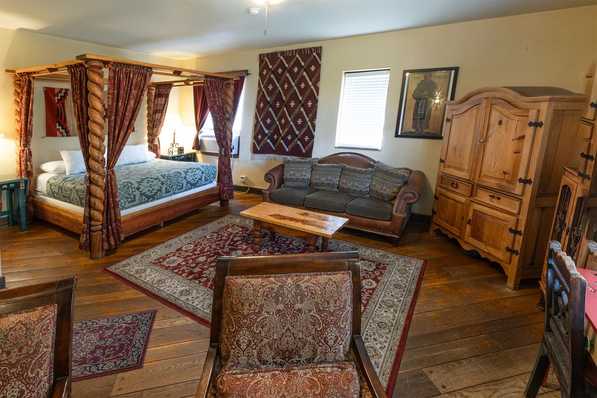 Bedroom with a four-poster bed, sofa, antique wooden wardrobe, chairs, and patterned rug.