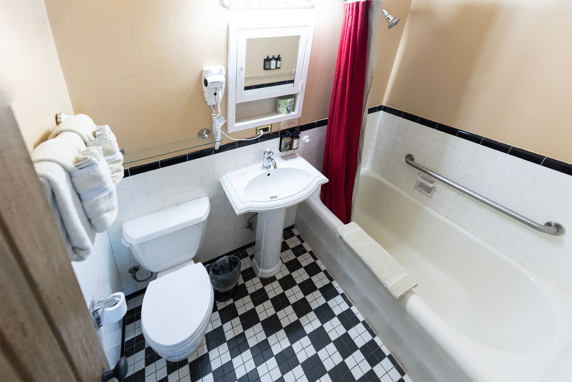 Small hotel bathroom with a toilet, sink, tub, and black and white checkered floor.