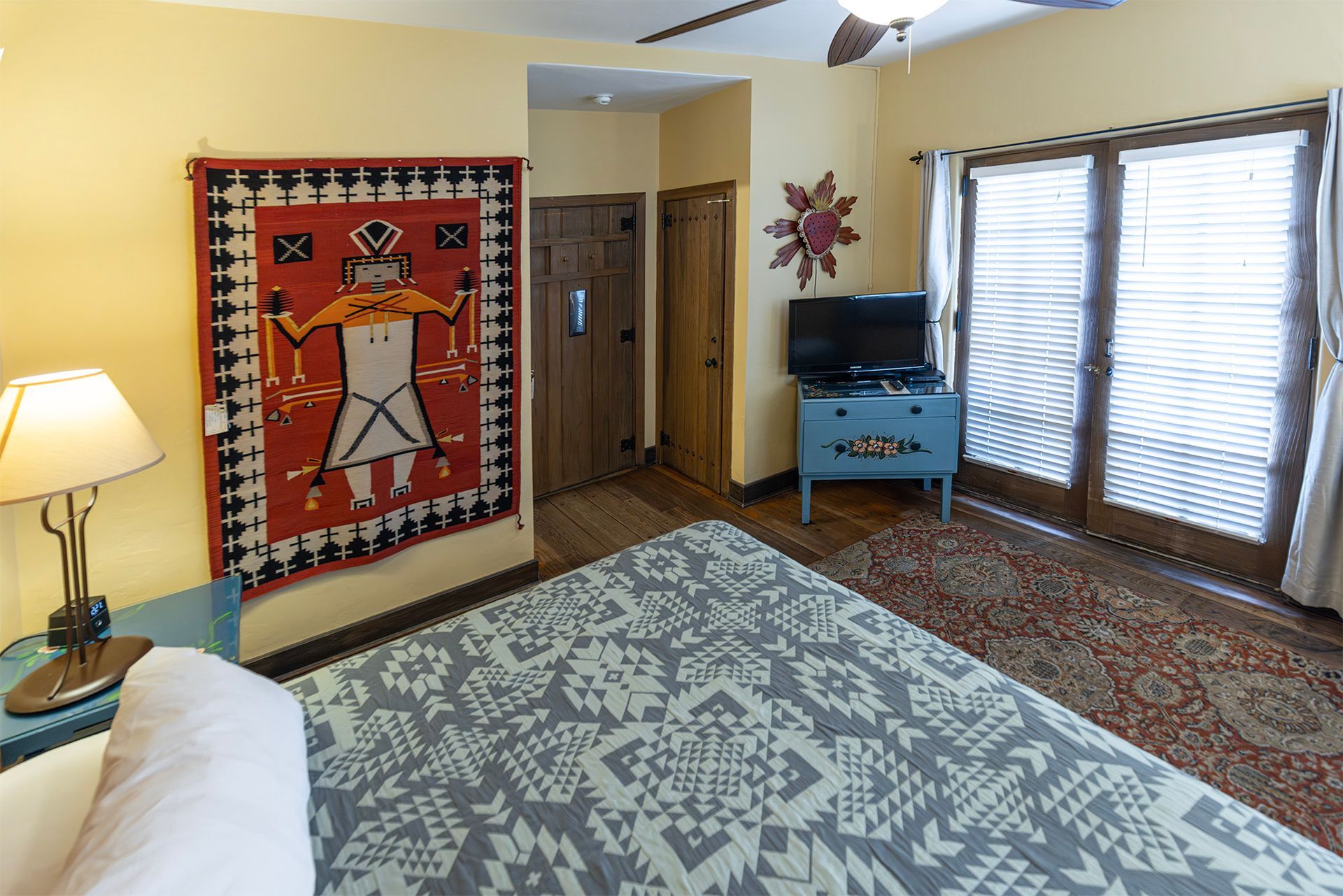 Bedroom with a bed, rug, painted dresser, and doors to a balcony. Native American wall hanging.