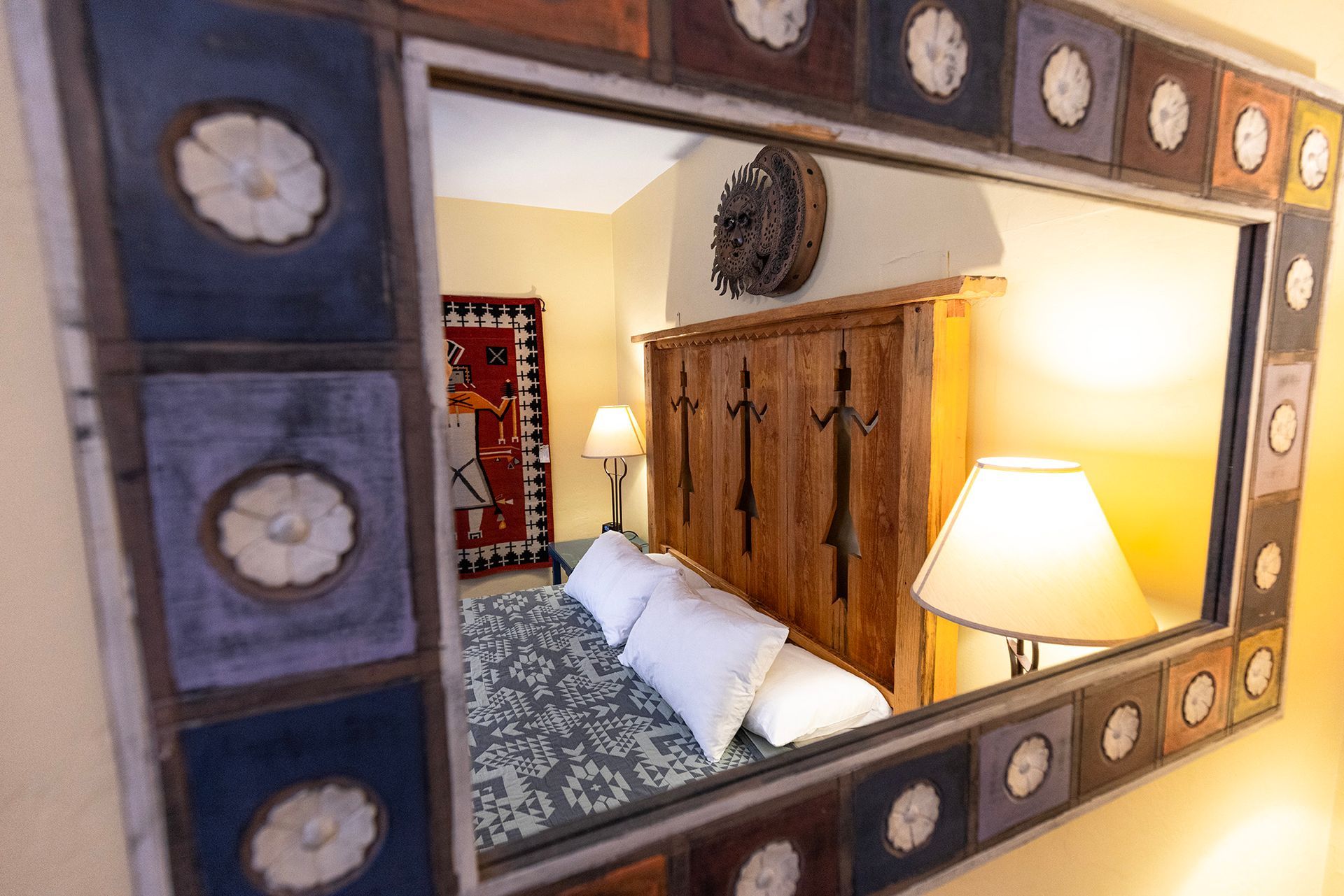 Mirror reflecting a bedroom with a bed, rug, lamps, and rustic wooden wardrobe.