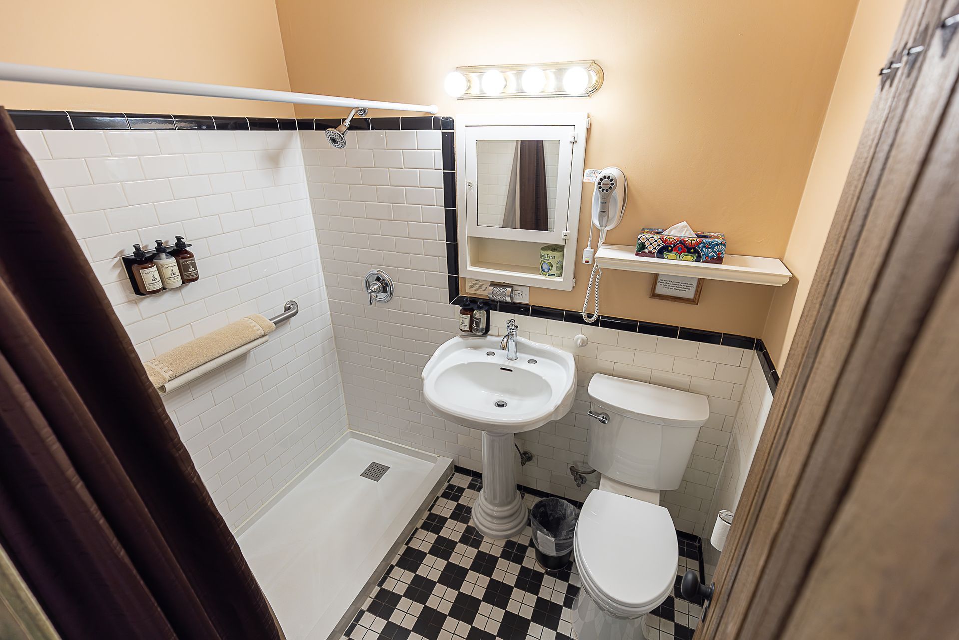 Small bathroom with pedestal sink, toilet, and shower. Black and white checkered floor, white tile.