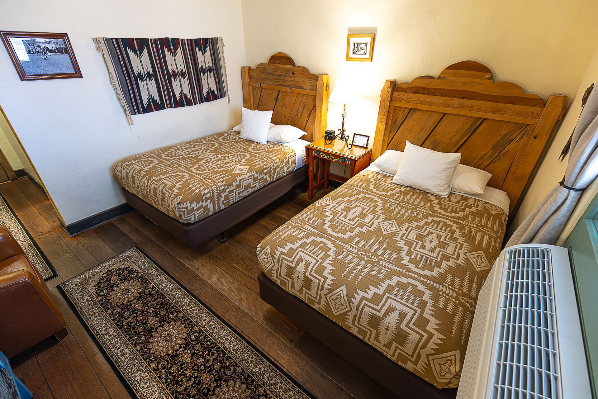 Two beds with wooden headboards in a hotel room. A rug and tapestry are on the walls.