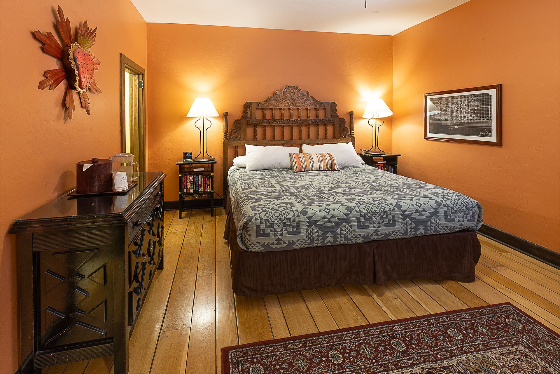 Bedroom with orange walls, wooden furniture, bed with floral comforter, and oriental rug.