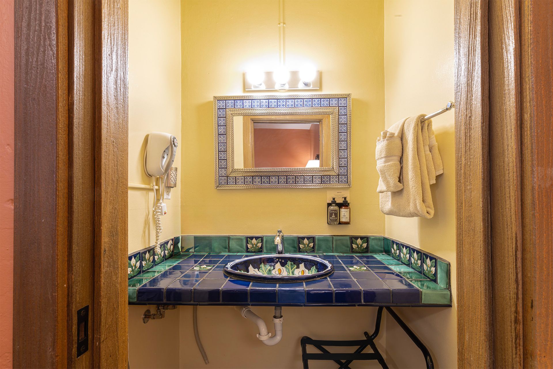 Bathroom with blue and green tiled vanity, mirror, towels, and hair dryer.