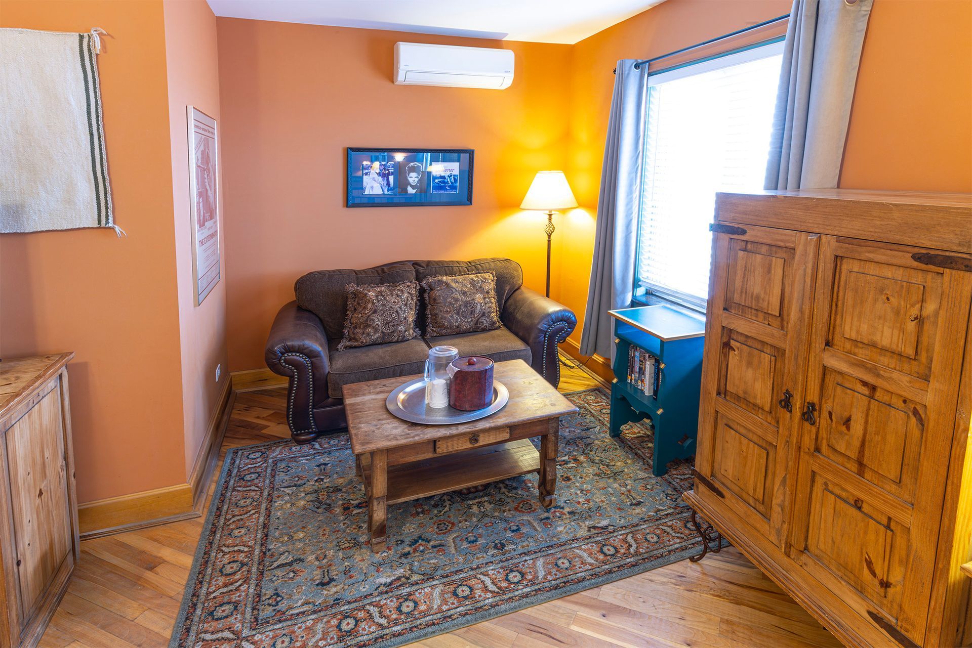 Cozy room with brown couch, wooden furniture, rug, and window. Orange walls.