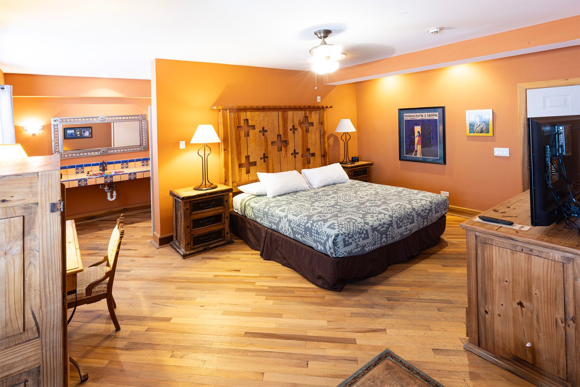 Bedroom with king bed, orange walls, wooden furniture, and a vanity with mirror.
