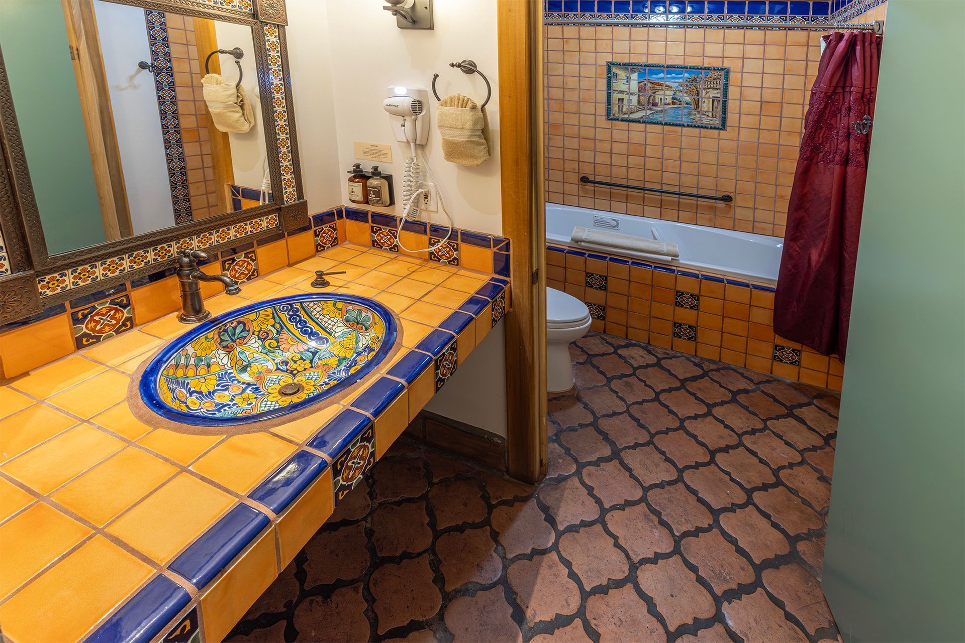 Bathroom with orange tiles, blue accents, ornate sink, and bathtub.