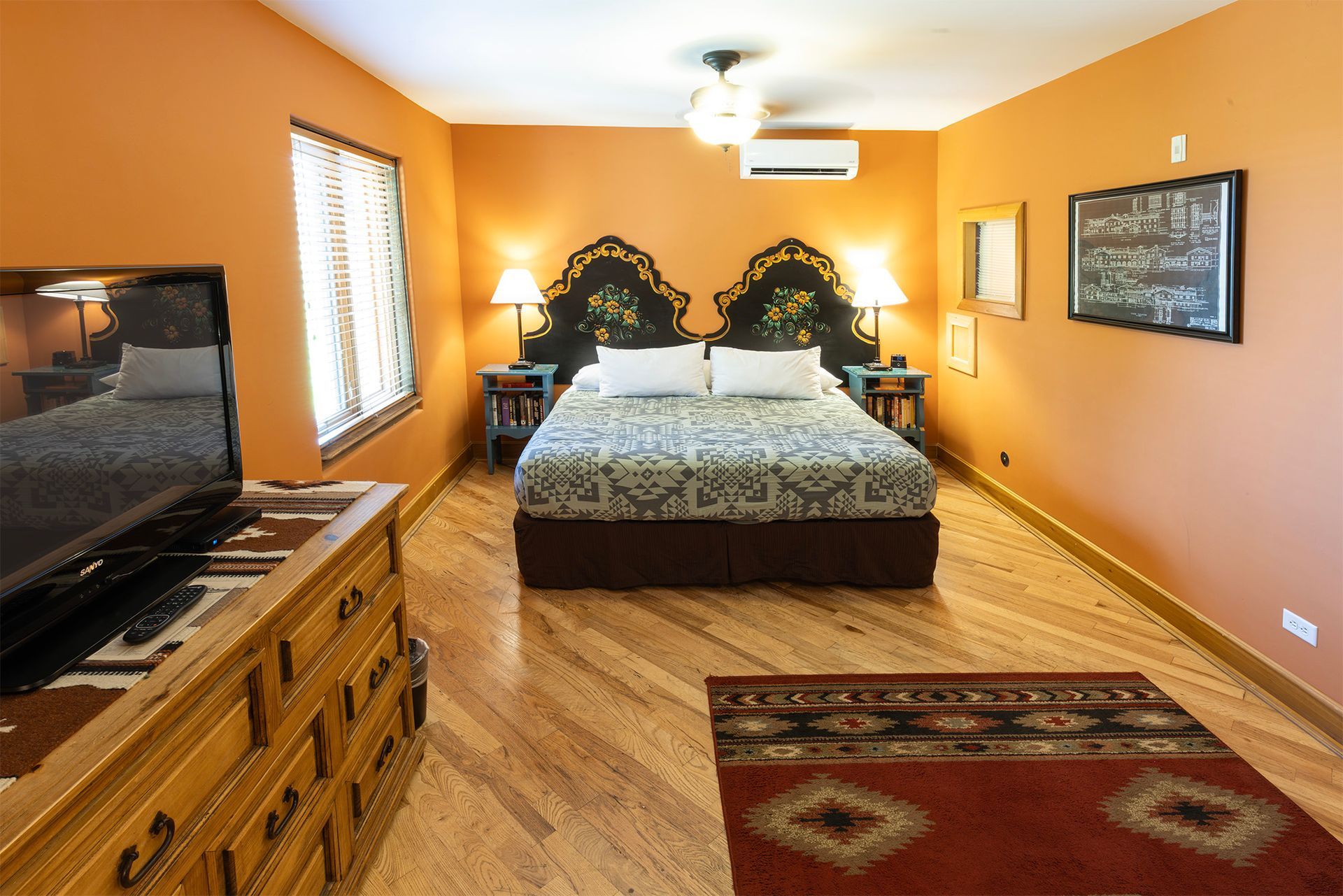 Bedroom with orange walls, hardwood floor, bed, dresser, rug, and two nightstands.