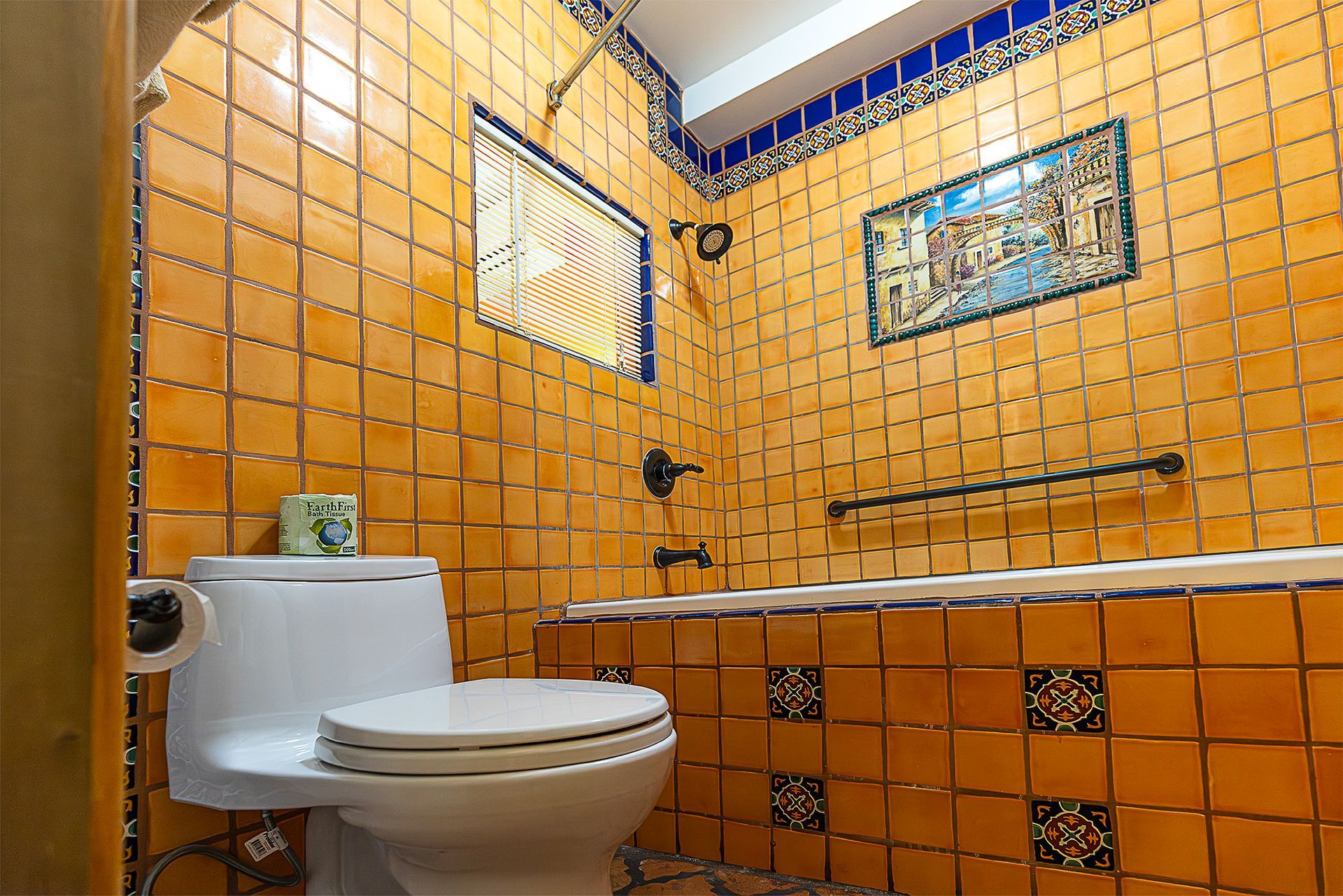 Bathroom with orange tile walls, white toilet, and a decorative cityscape painting.